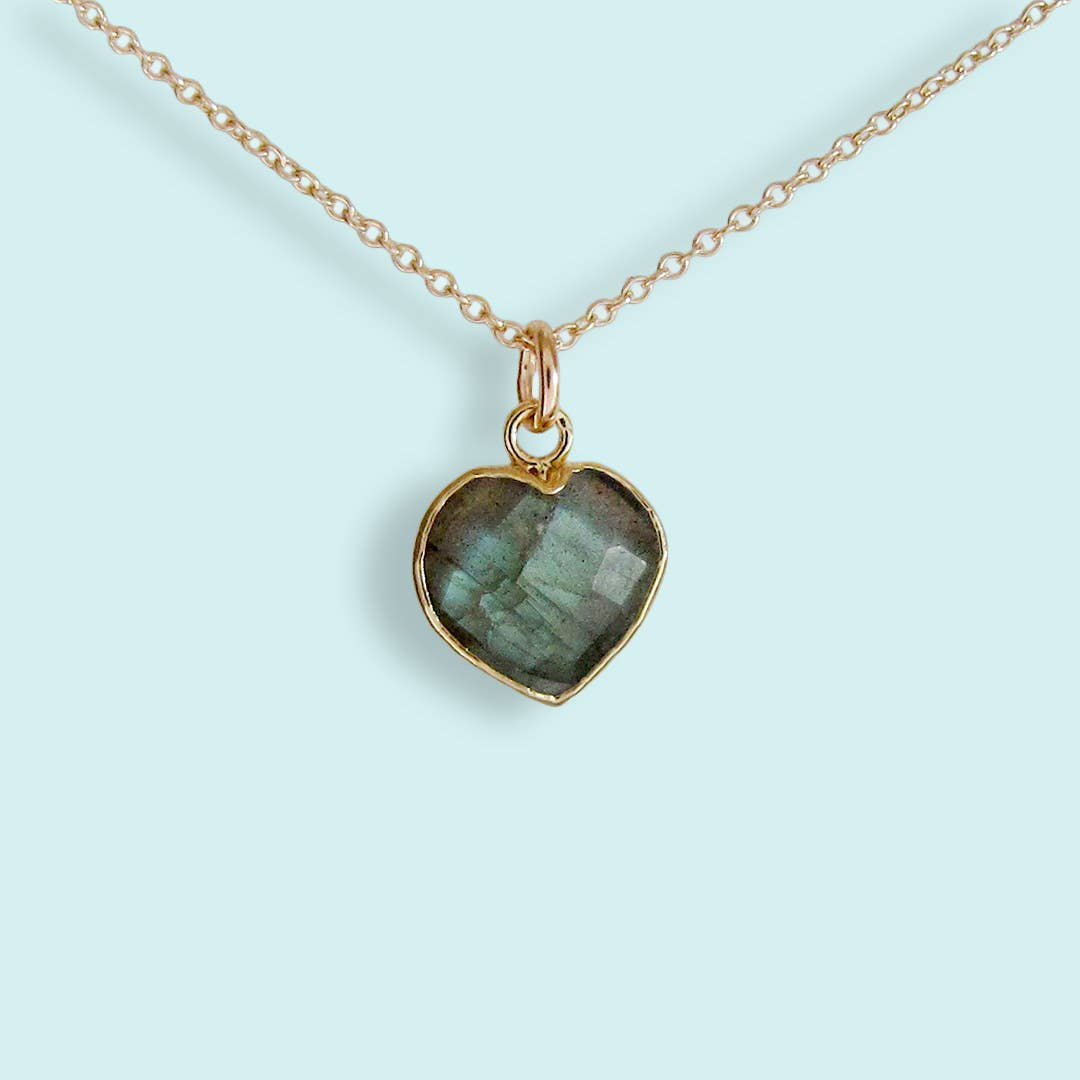 Heart-shaped pendant with green stone on a gold chain against a light blue background