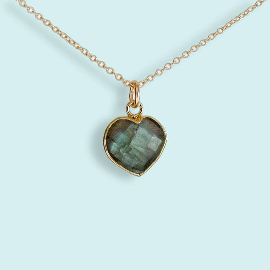Heart-shaped pendant with green stone on a gold chain against a light blue background