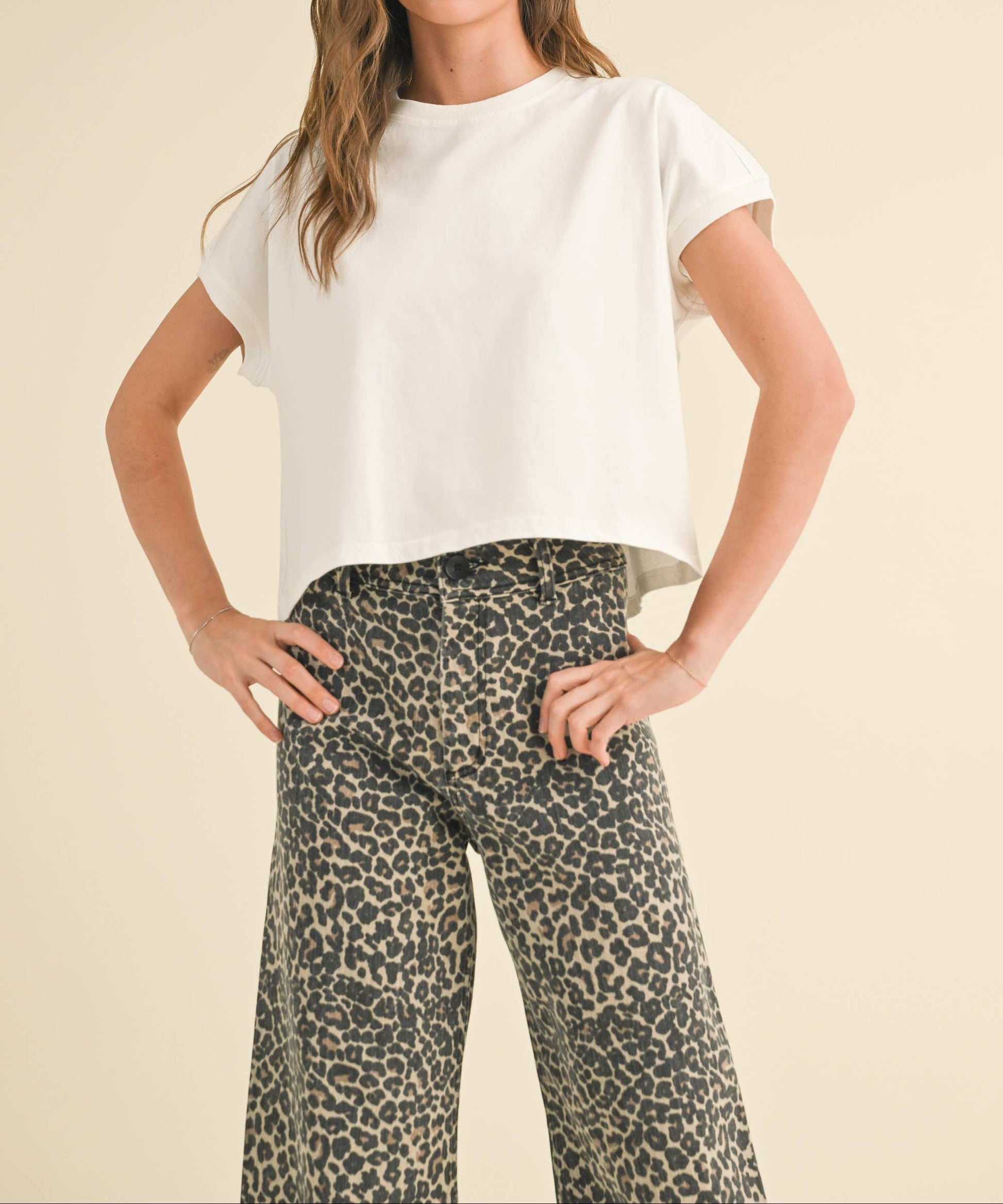 Woman wearing a white top and leopard print pants against a beige background