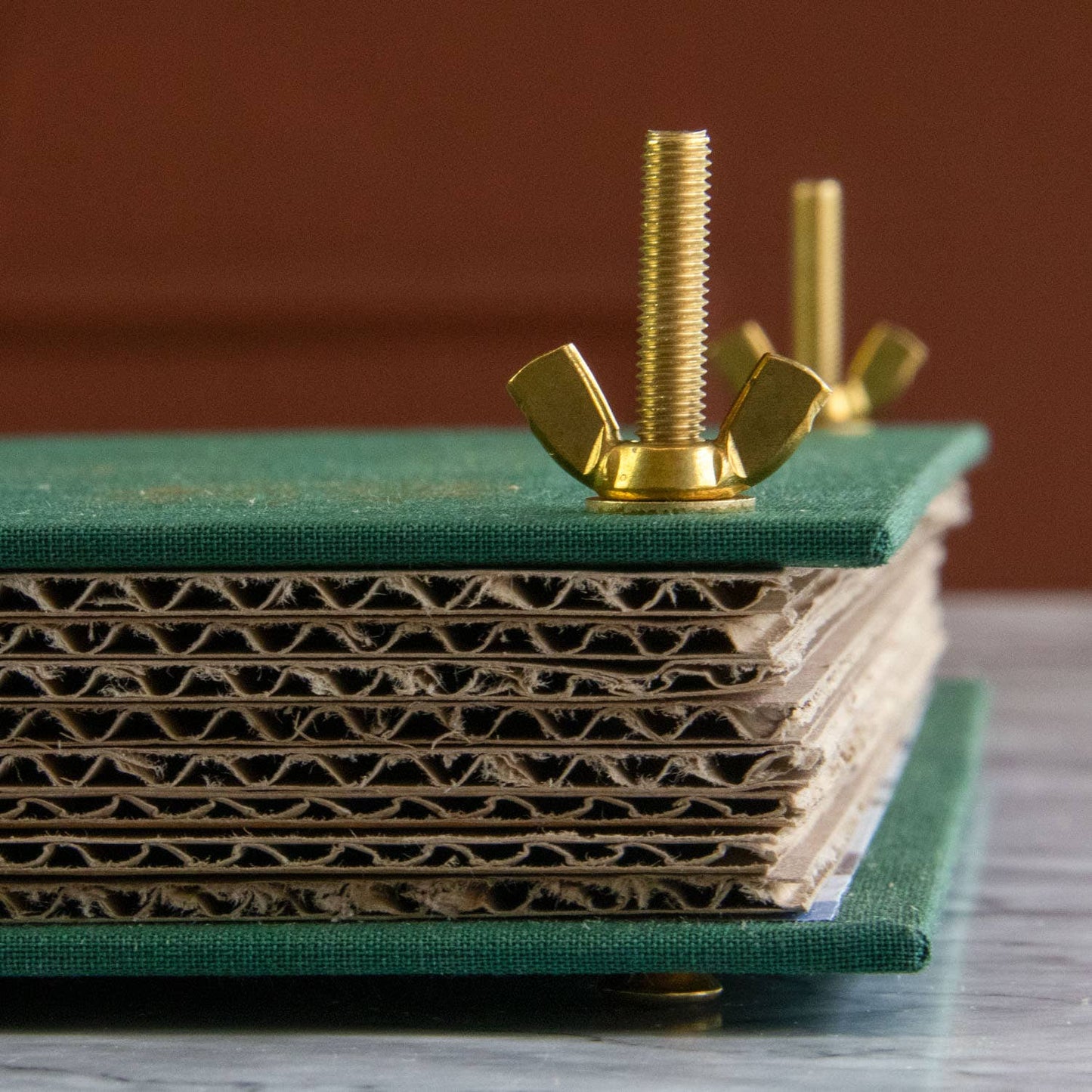Gold wingnut and bolt on a stack of green cardboard boxes with a brown background