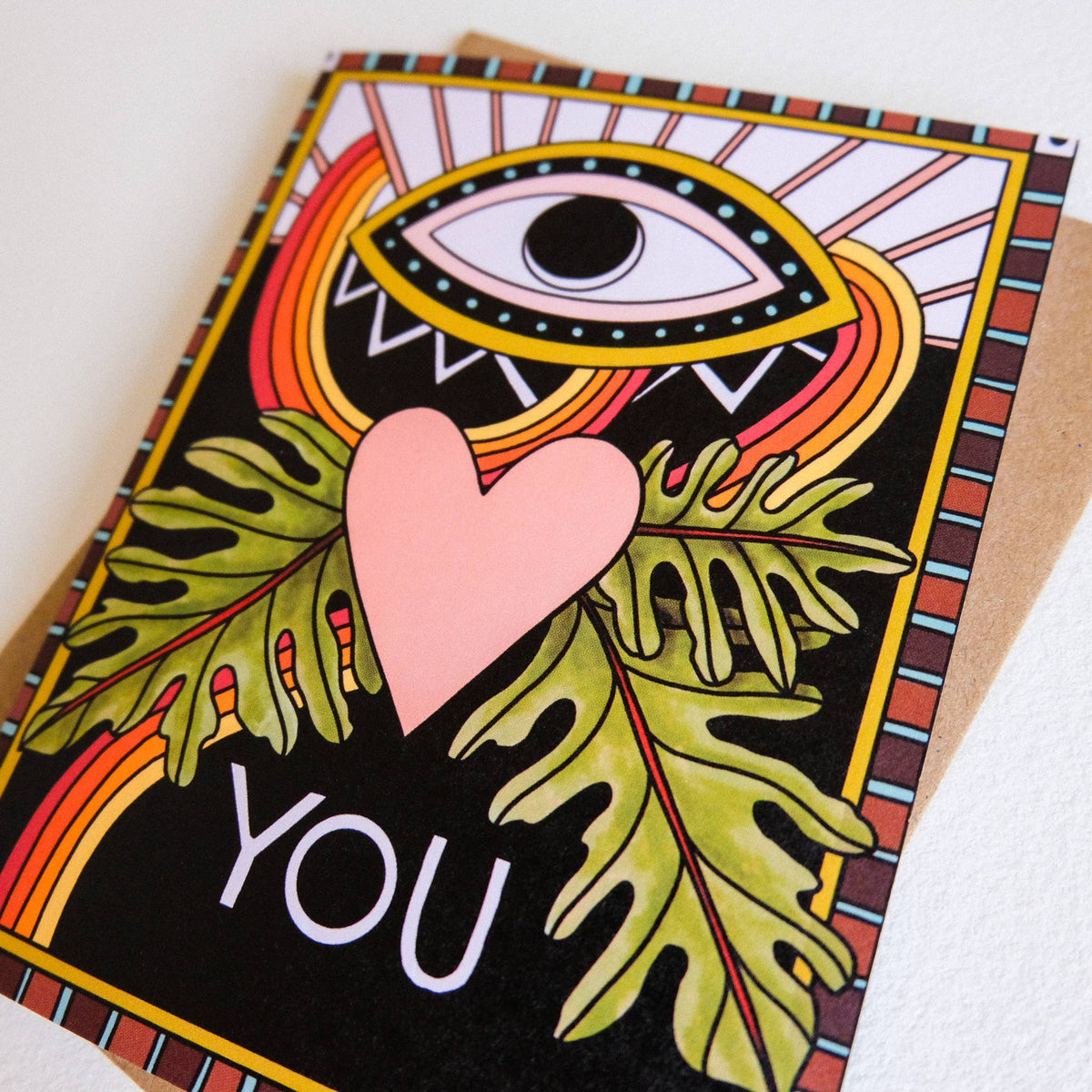 Greeting card with eye design, leaves, and heart, featuring the word 'YOU'.