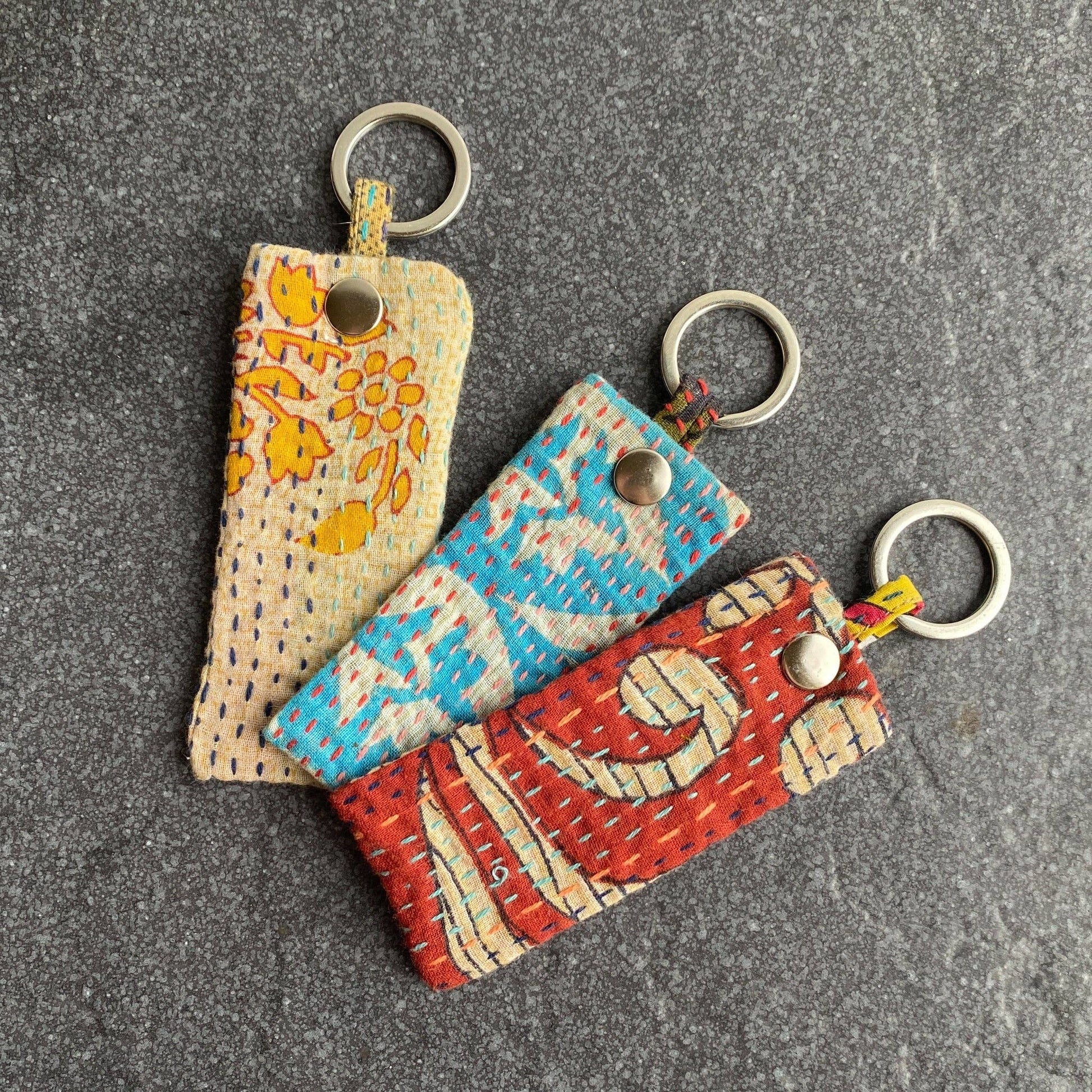 Three colorful keychains with patterned fabric on a gray surface