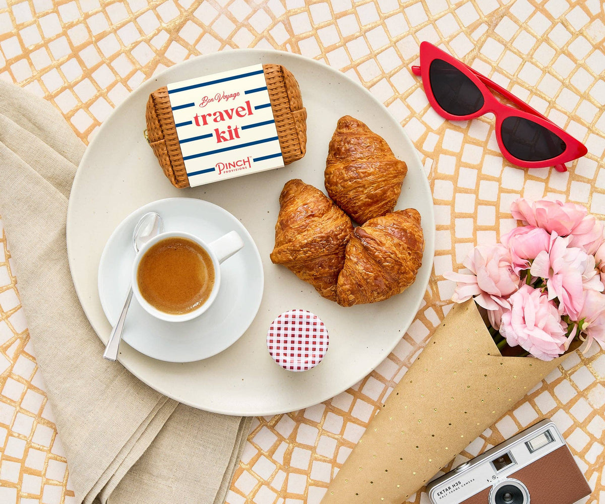 Breakfast setting with coffee, croissants, and travel kit on a tablecloth.