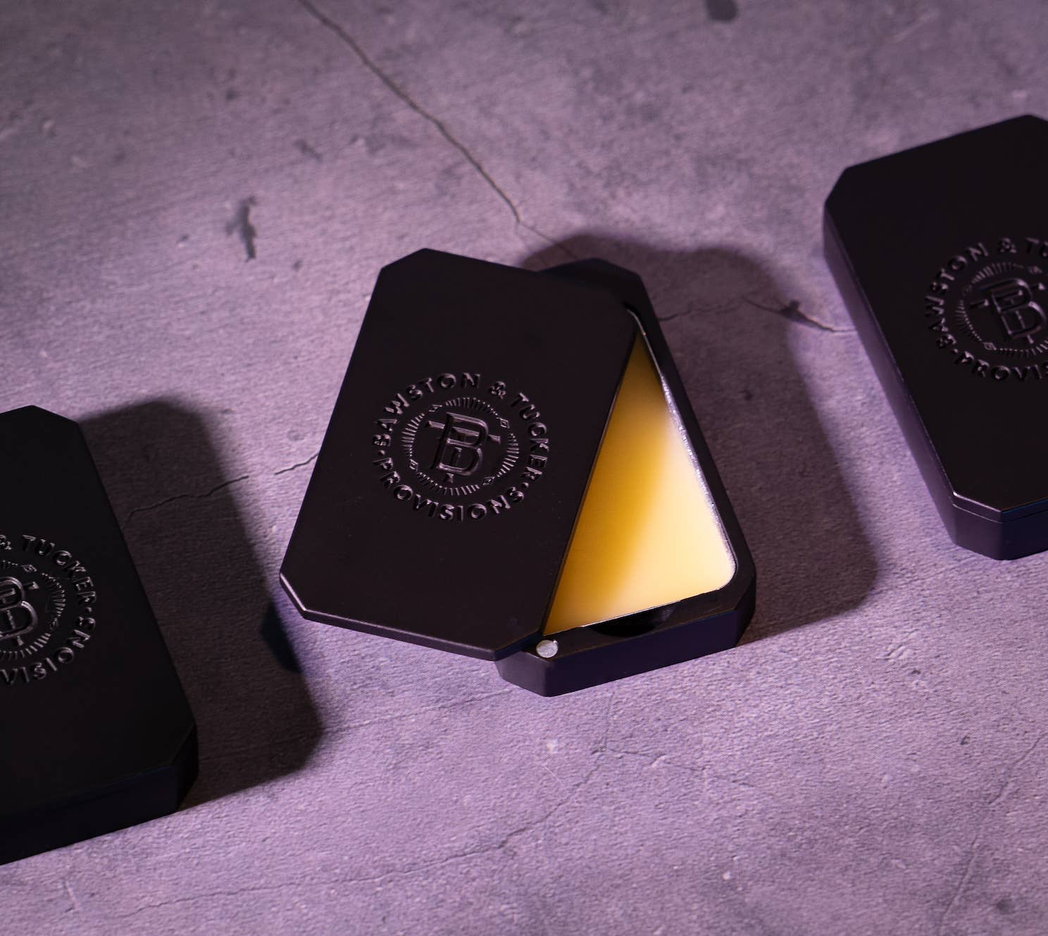 Black containers with a yellow substance inside on a gray surface, featuring a logo.
