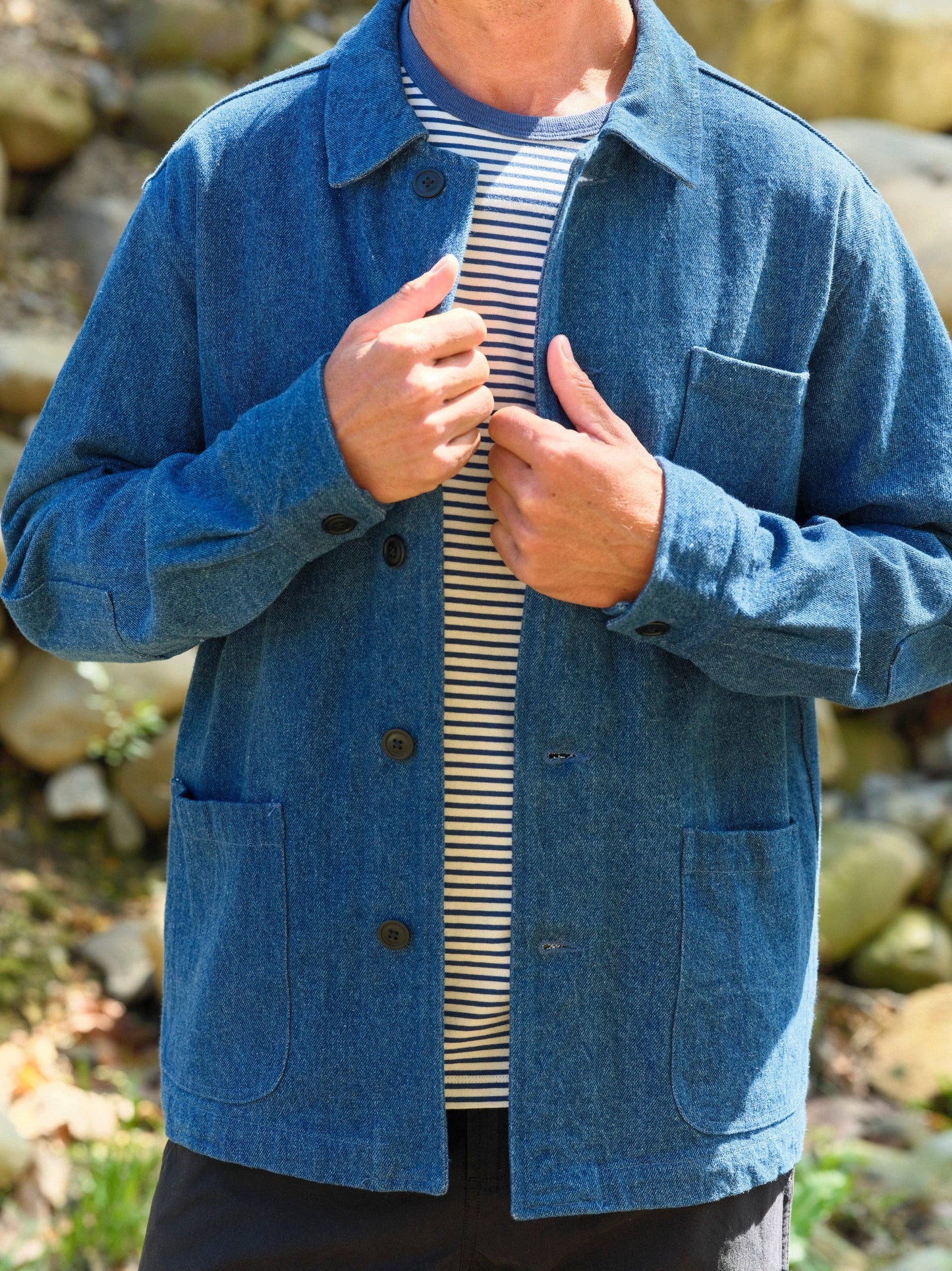 Person wearing a blue jacket over a striped shirt with a natural background