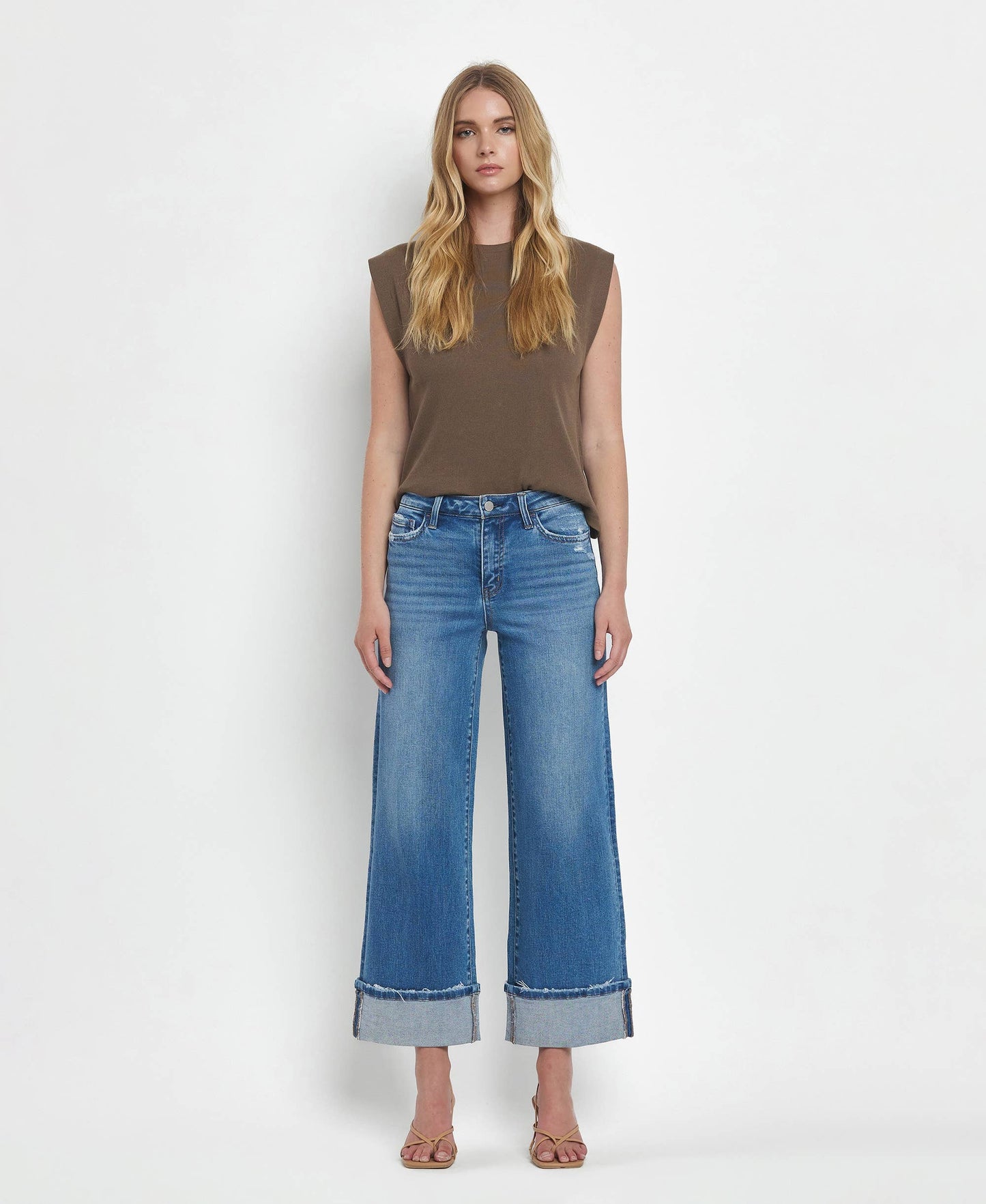 Woman wearing a brown sleeveless top and blue jeans on a white background
