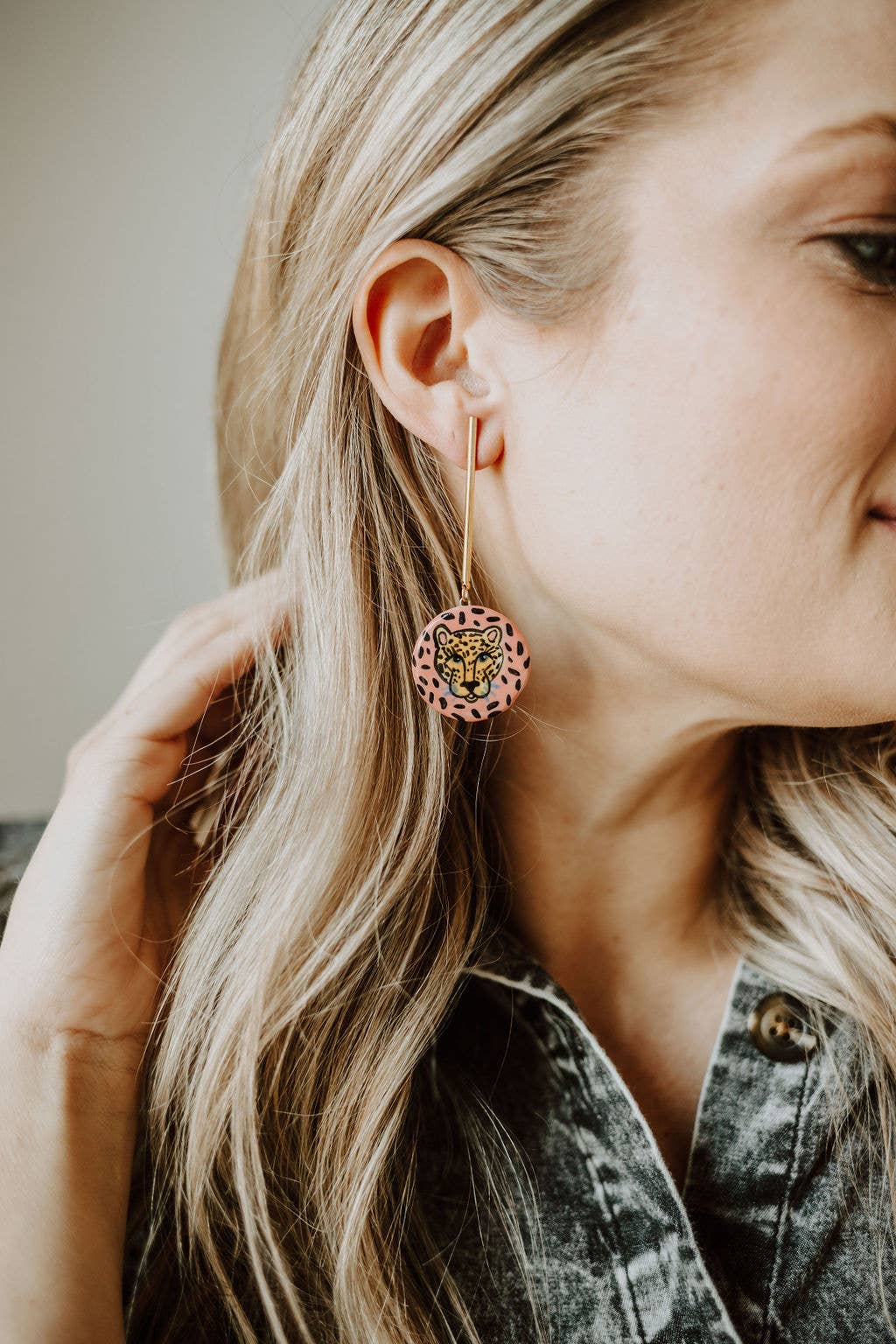 Close-up of a person wearing pink earrings with a lion design.