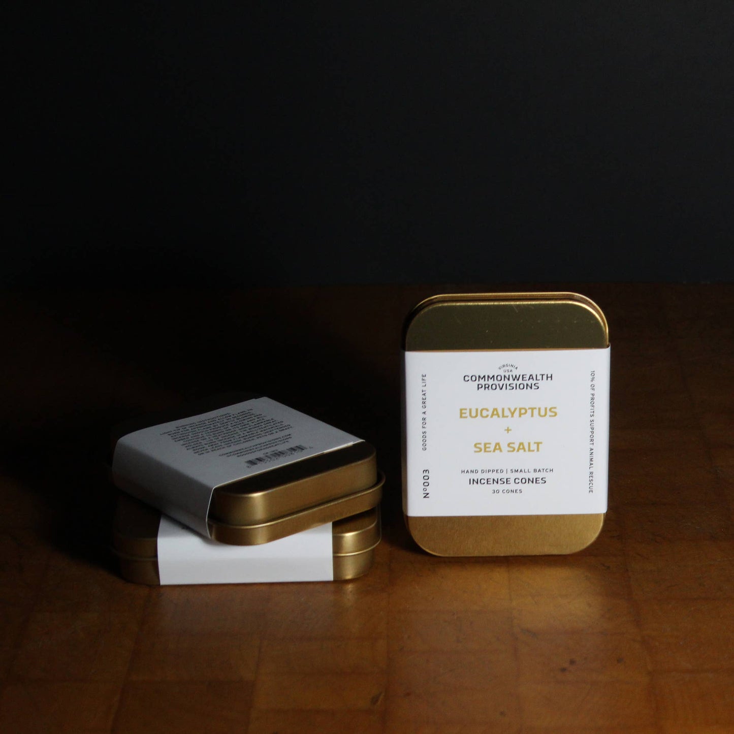 Two tins, one gold and one white, on a wooden surface with a dark background.