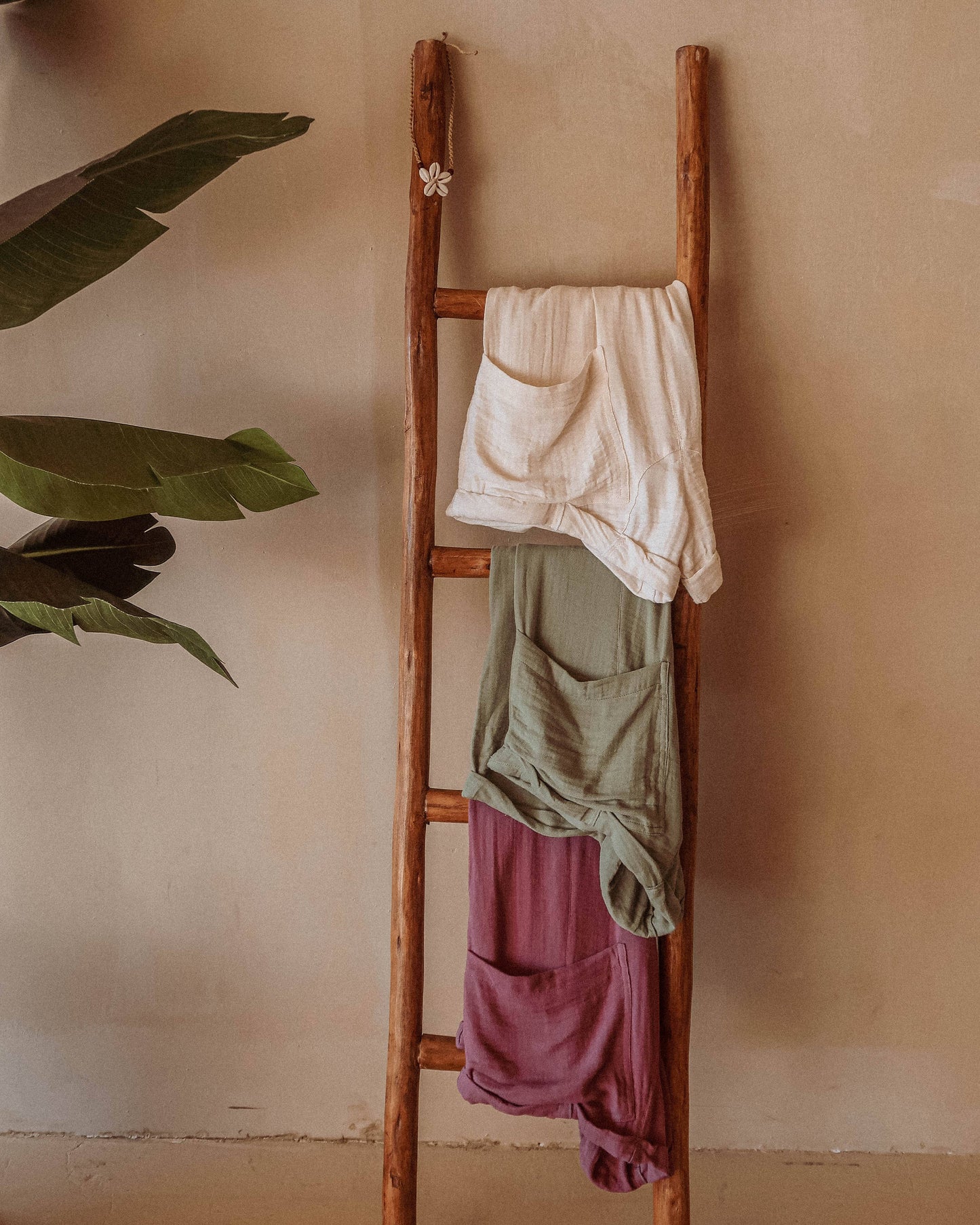 Wooden ladder with hanging clothes against a beige wall