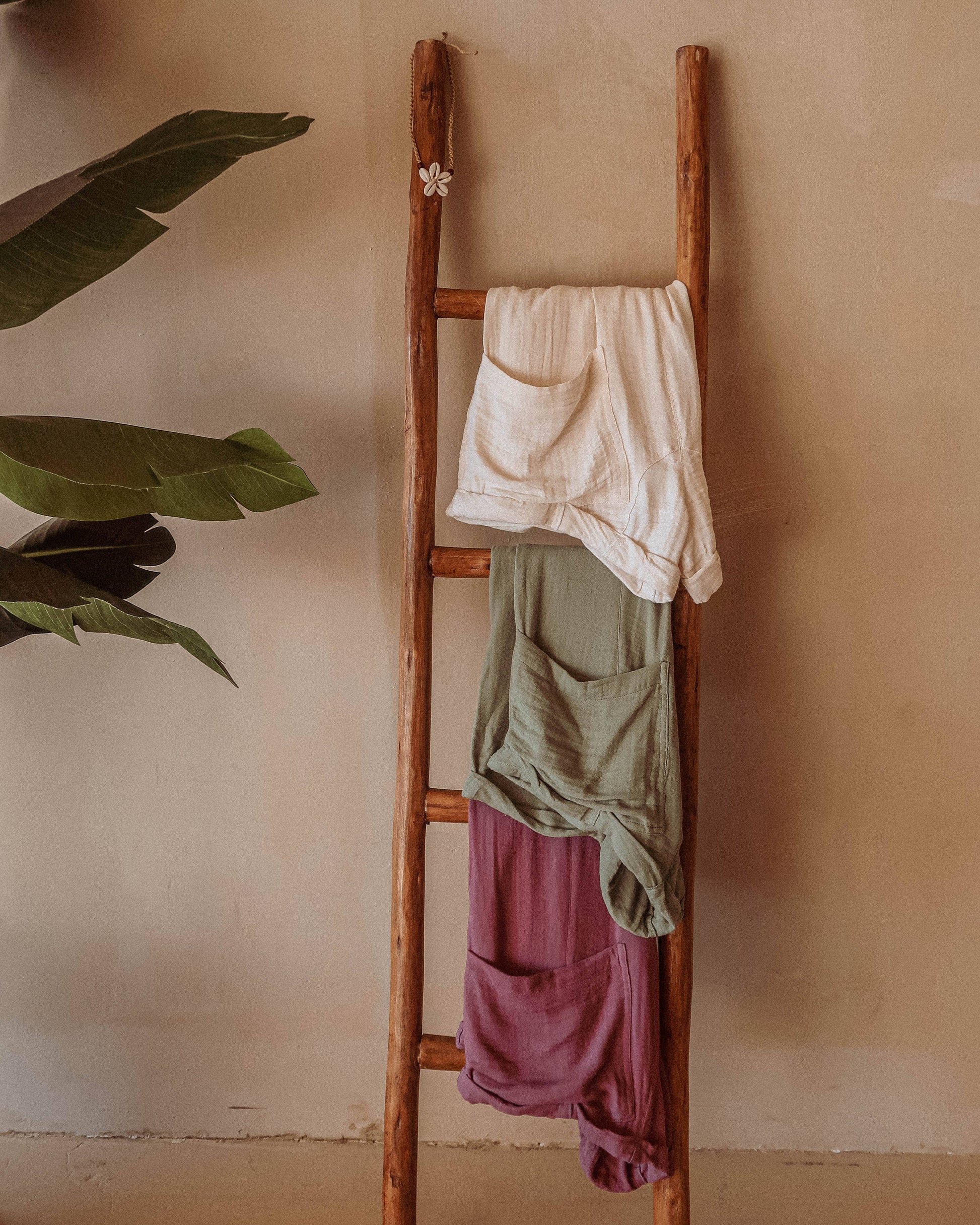 Wooden ladder with hanging clothes against a beige wall