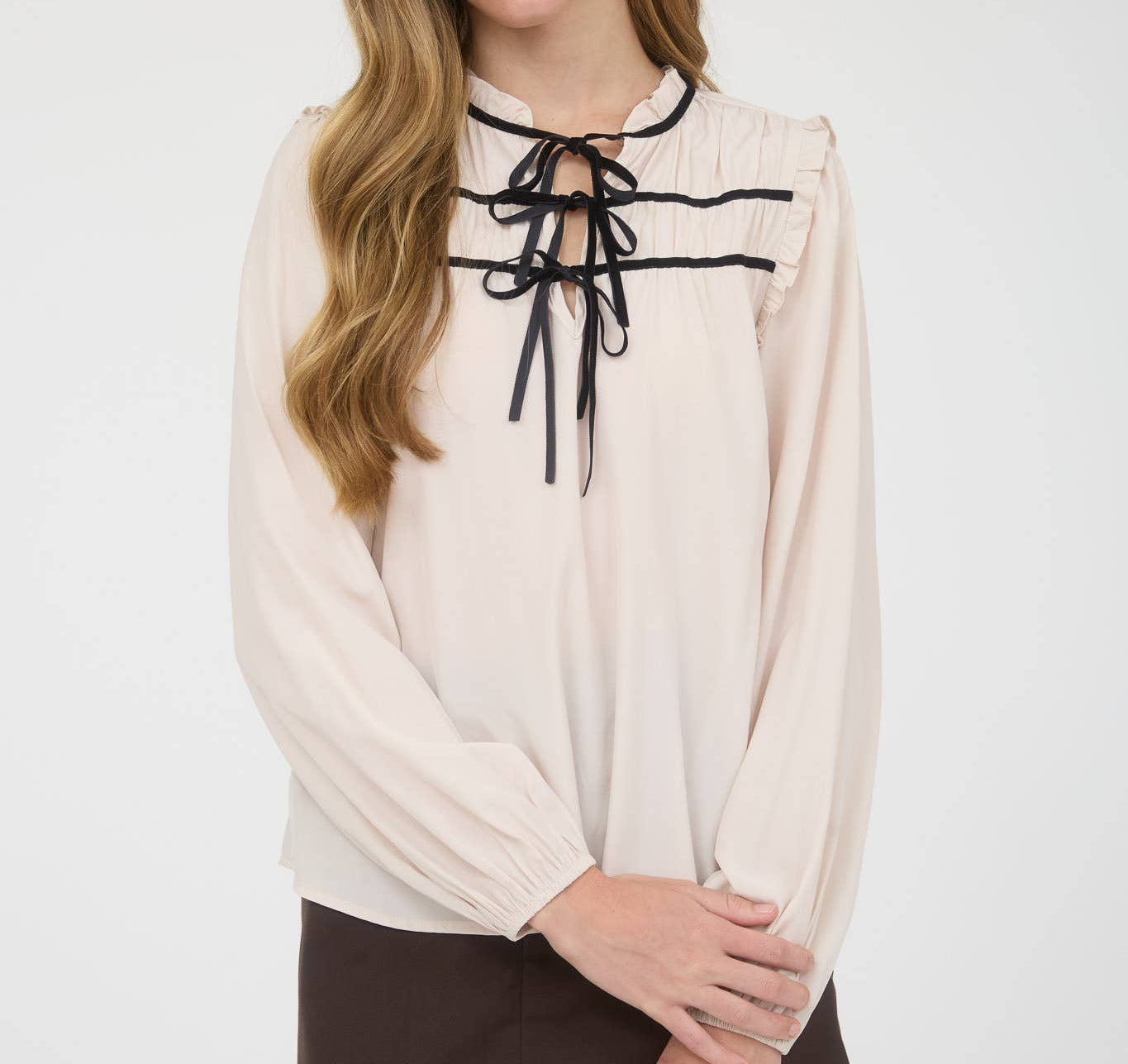 Woman wearing a beige blouse with black ribbon details on a white background