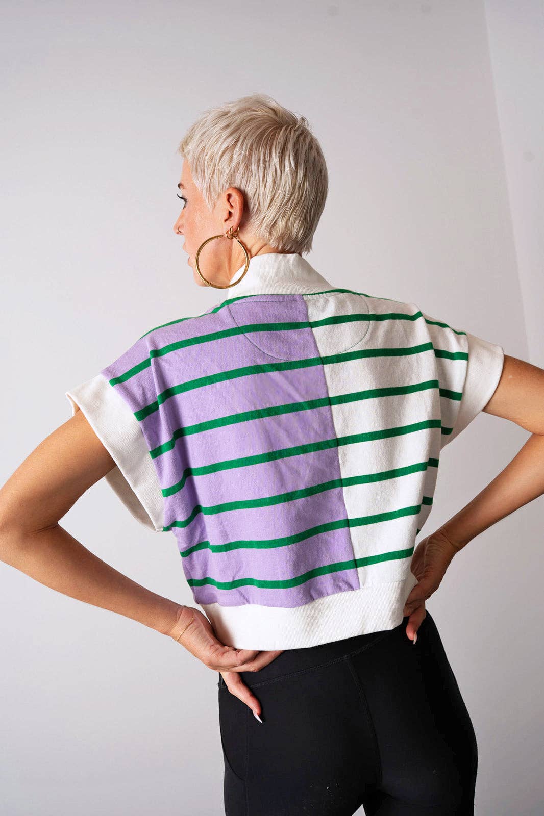 Person wearing a striped shirt with purple, green, and white pattern on a plain background