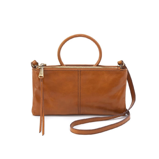 A tan leather handbag with a top handle, a zippered top closure, a side tassel pull, and an adjustable shoulder strap, shown against a plain white background.