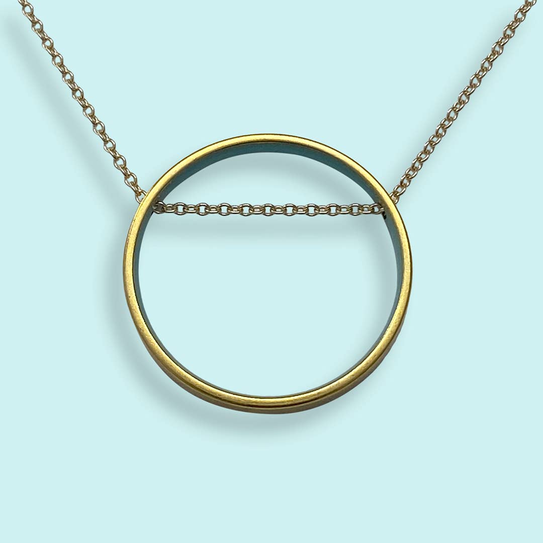 Gold circular pendant necklace on a light blue background
