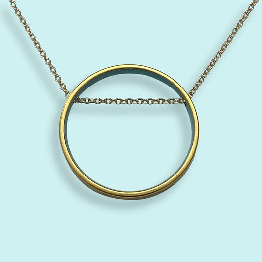 Gold circular pendant necklace on a light blue background