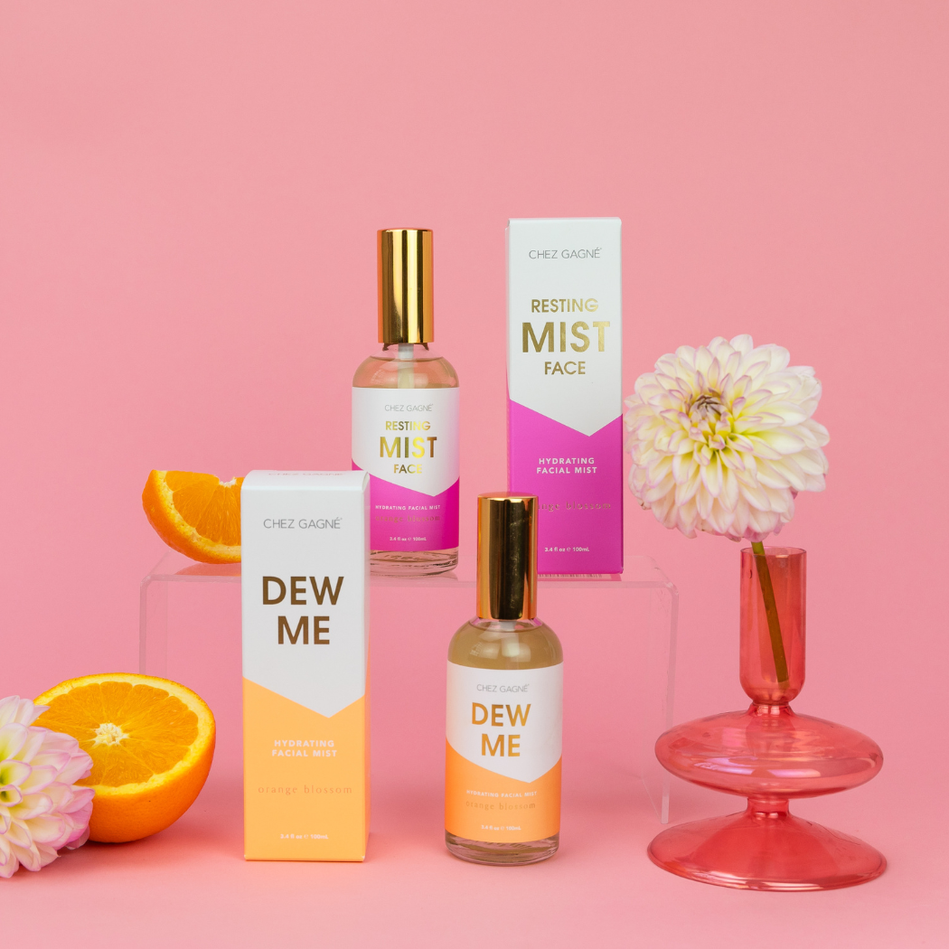 Cheri Gaine skincare products with oranges and flowers on a pink background