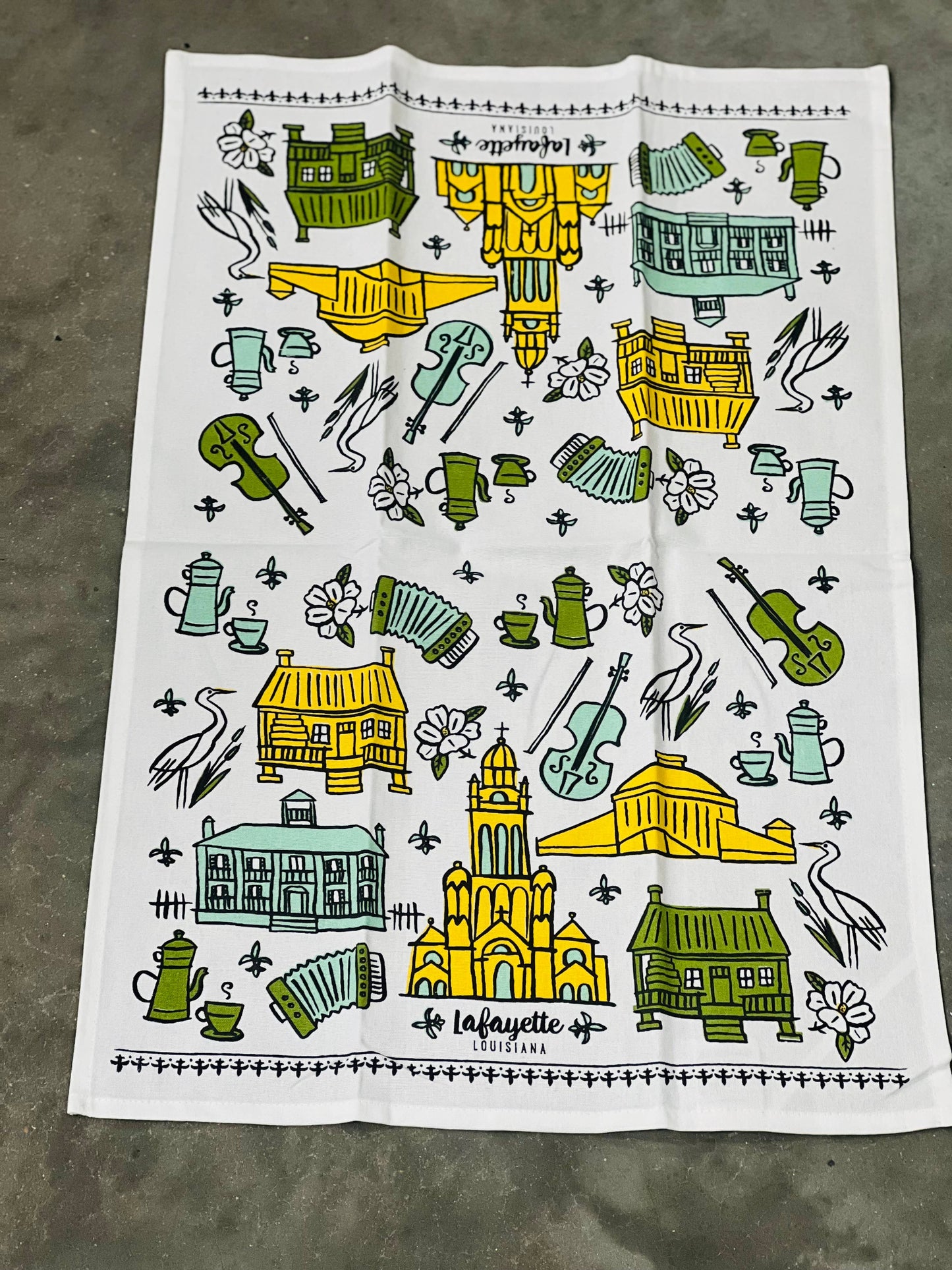 Decorative towel with artistic illustrations of buildings, furniture, and other objects on a concrete surface.