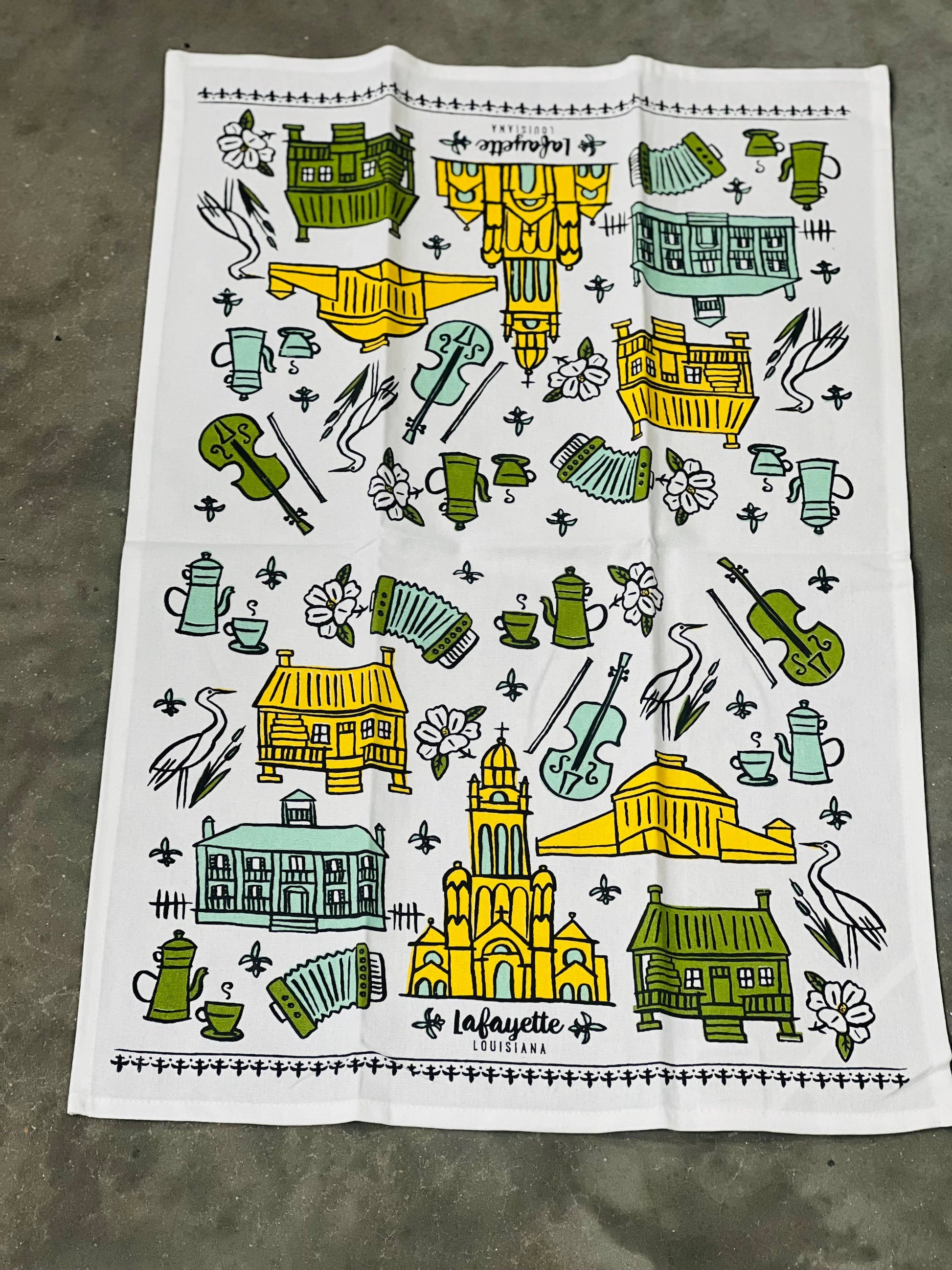 Decorative towel with artistic illustrations of buildings, furniture, and other objects on a concrete surface.