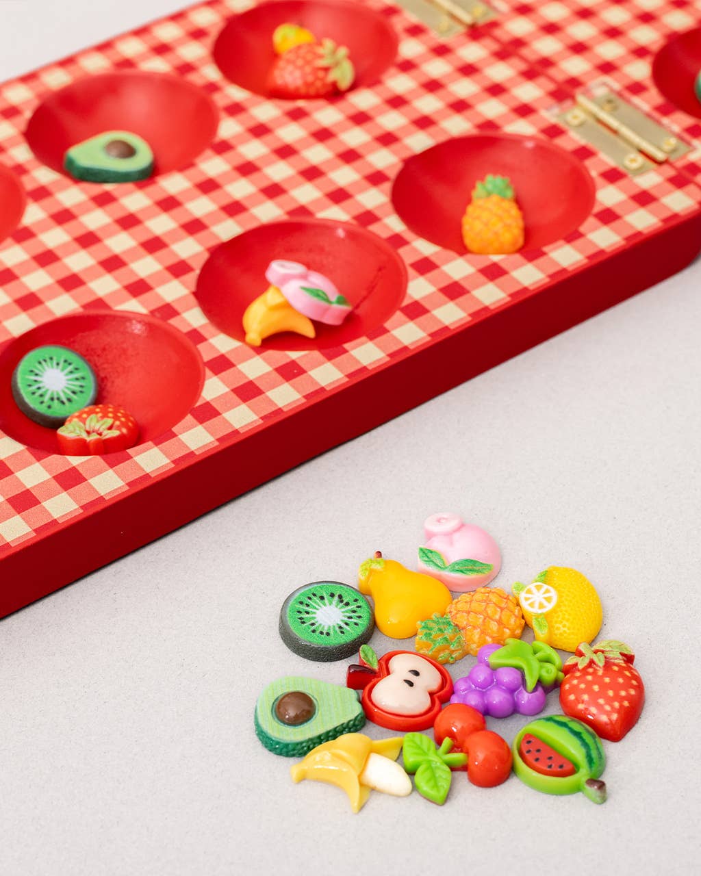 Colorful fruit-shaped candies on a red checkered board with additional candies on a white surface.