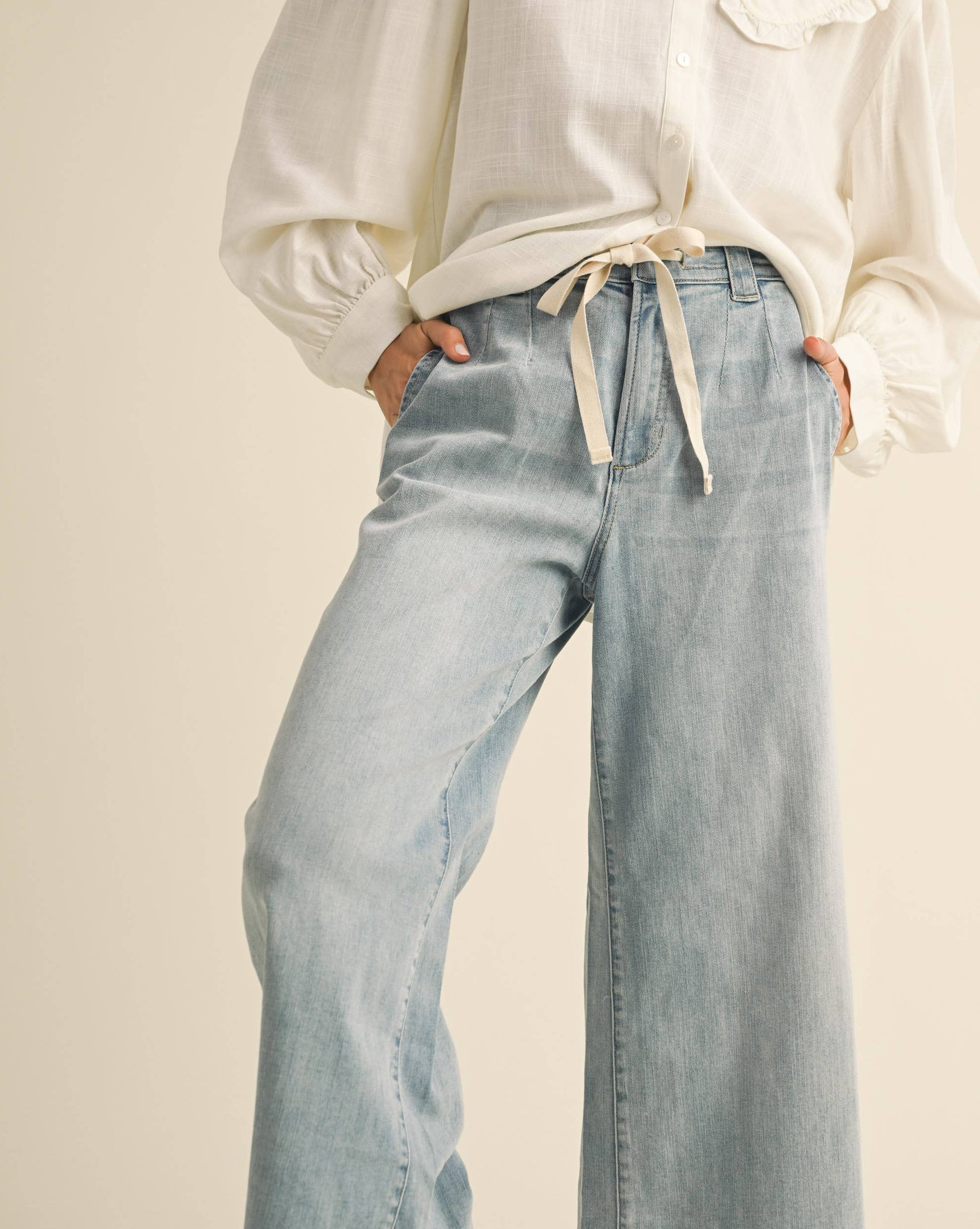 Person wearing a white blouse with a ruffled collar and light blue jeans on a beige background