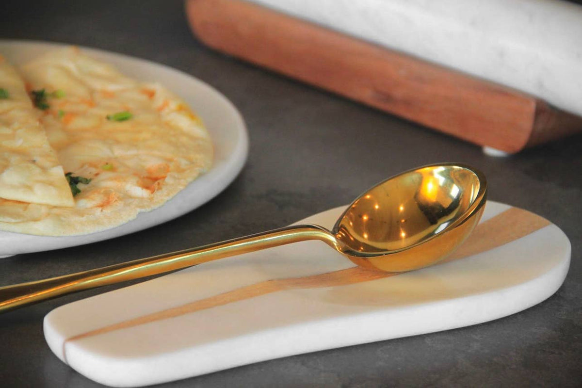 Gold spoon on a marble coaster with a plate of food in the background