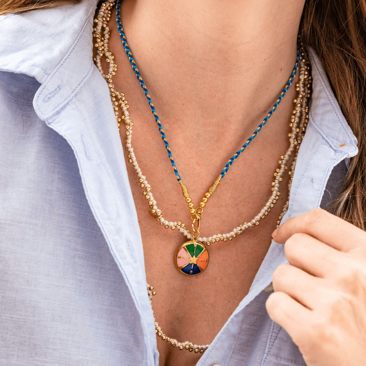 Close-up of a person wearing a colorful necklace with a blue cord and gold chain.
