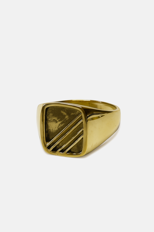 A gold signet ring with a square face featuring diagonal engraved lines, photographed on a clean, light gray background.