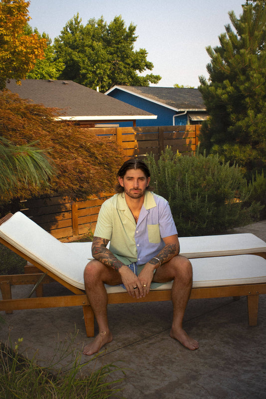 Man sitting on a lounge chair in a backyard setting with trees and a blue shed in the background.