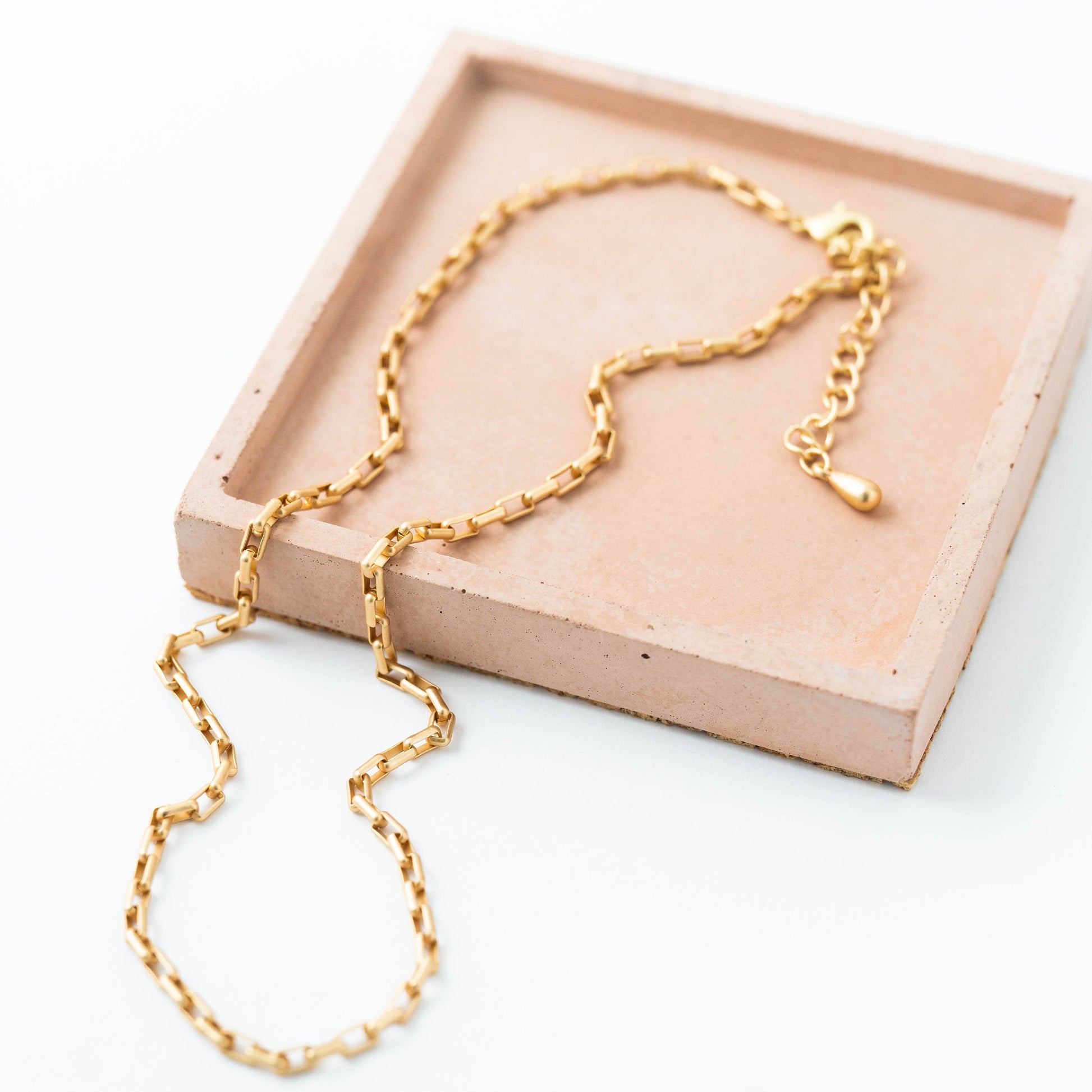 Gold chain necklace on a pink tray with a white background