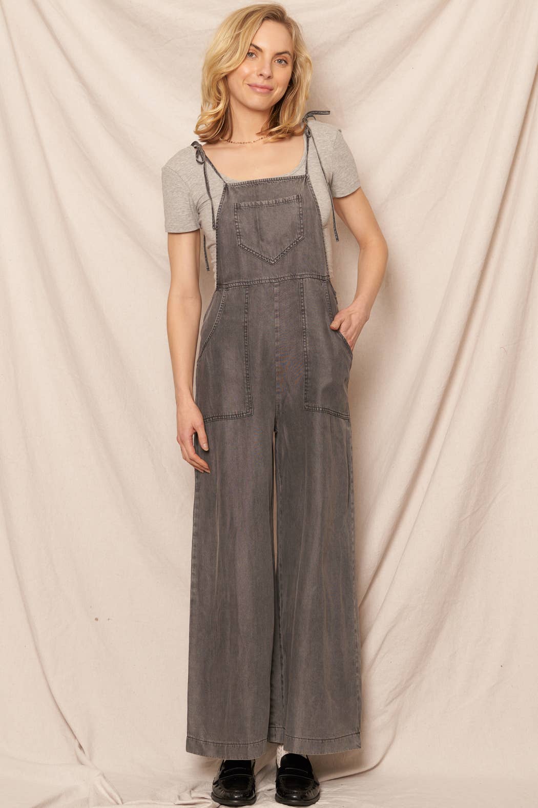 Woman wearing gray denim overalls against a plain background