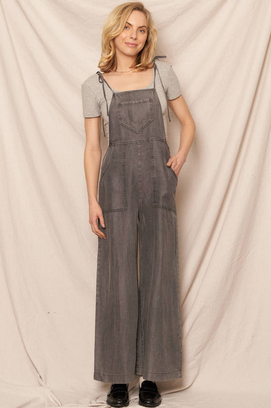 Woman wearing gray denim overalls against a plain background