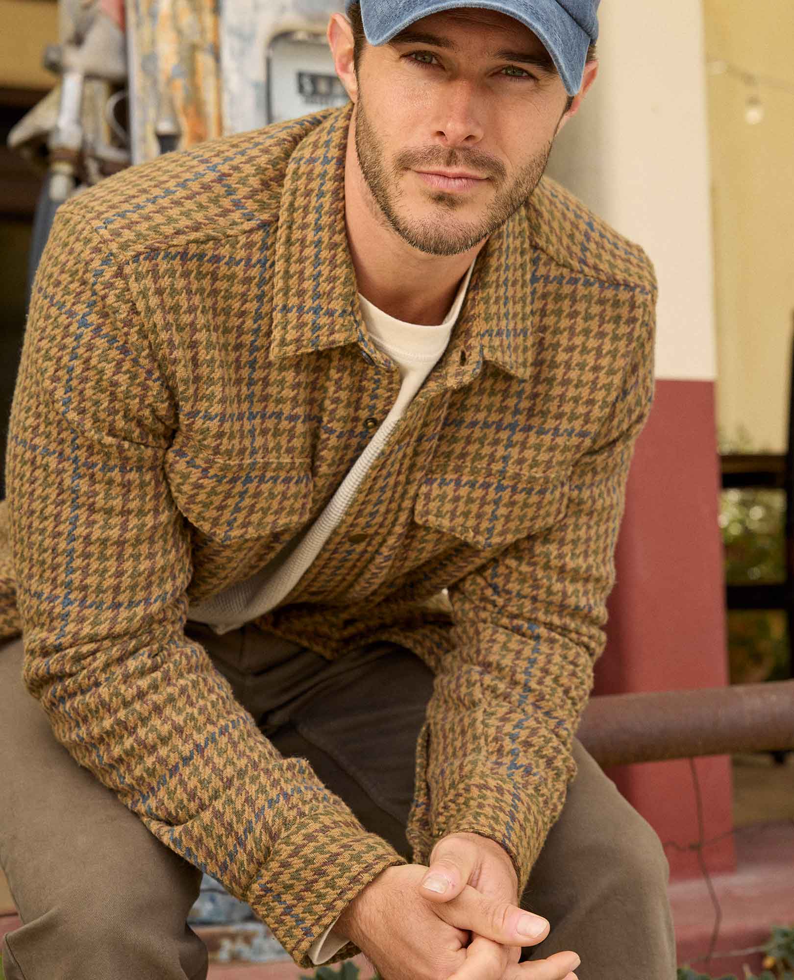 Man wearing a brown plaid jacket and cap in an outdoor setting