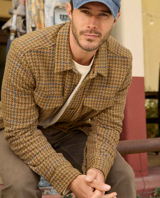 Man wearing a brown plaid jacket and cap in an outdoor setting