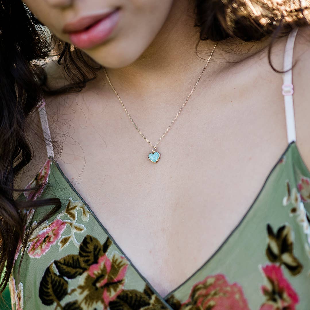 Close-up of a woman wearing a floral top and a delicate necklace with a heart-shaped pendant.
