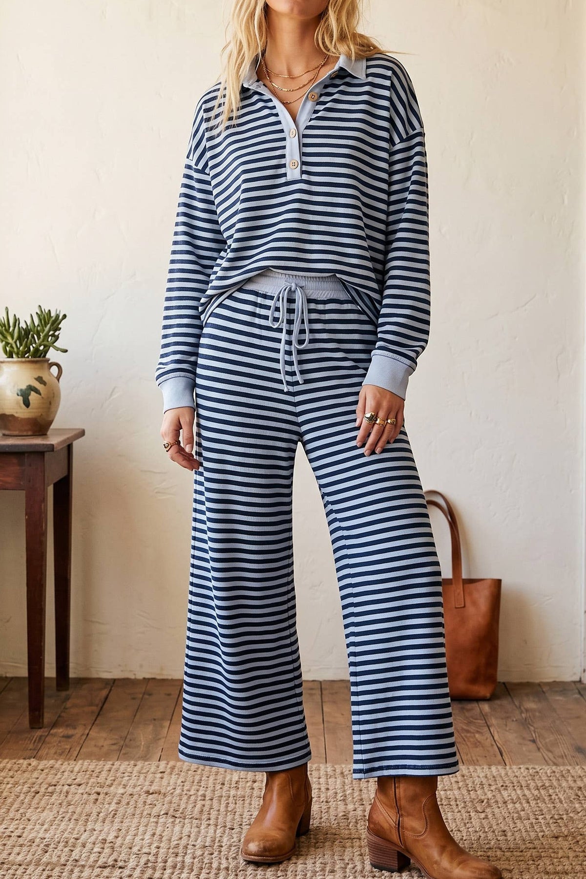 Woman wearing a blue and white striped outfit standing in a room with a wooden table and plants.