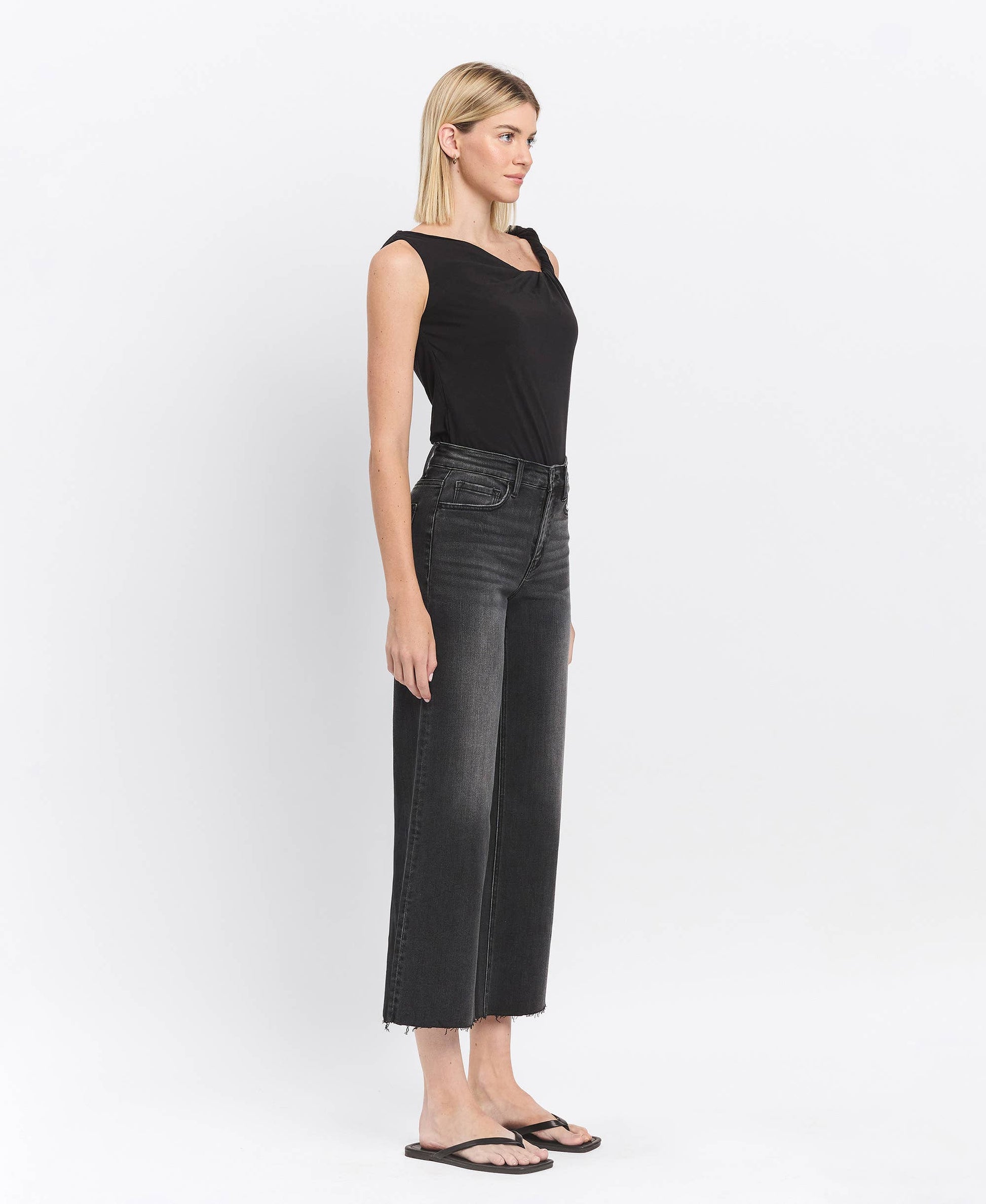 Woman wearing black sleeveless top and black jeans on a white background