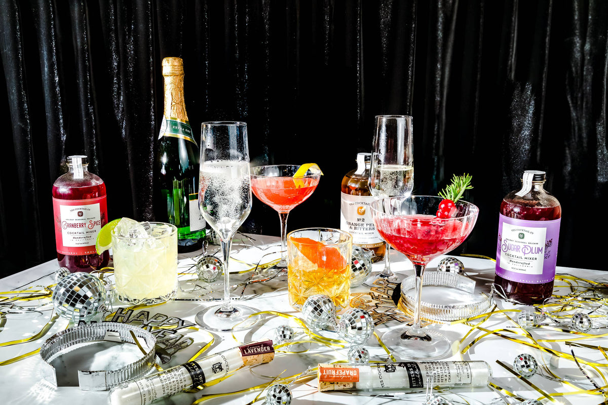 Table with various cocktails, bottles, and bar tools against a black curtain background