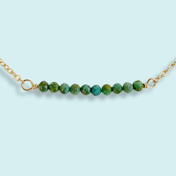 Green beaded necklace with gold chain on a light blue background