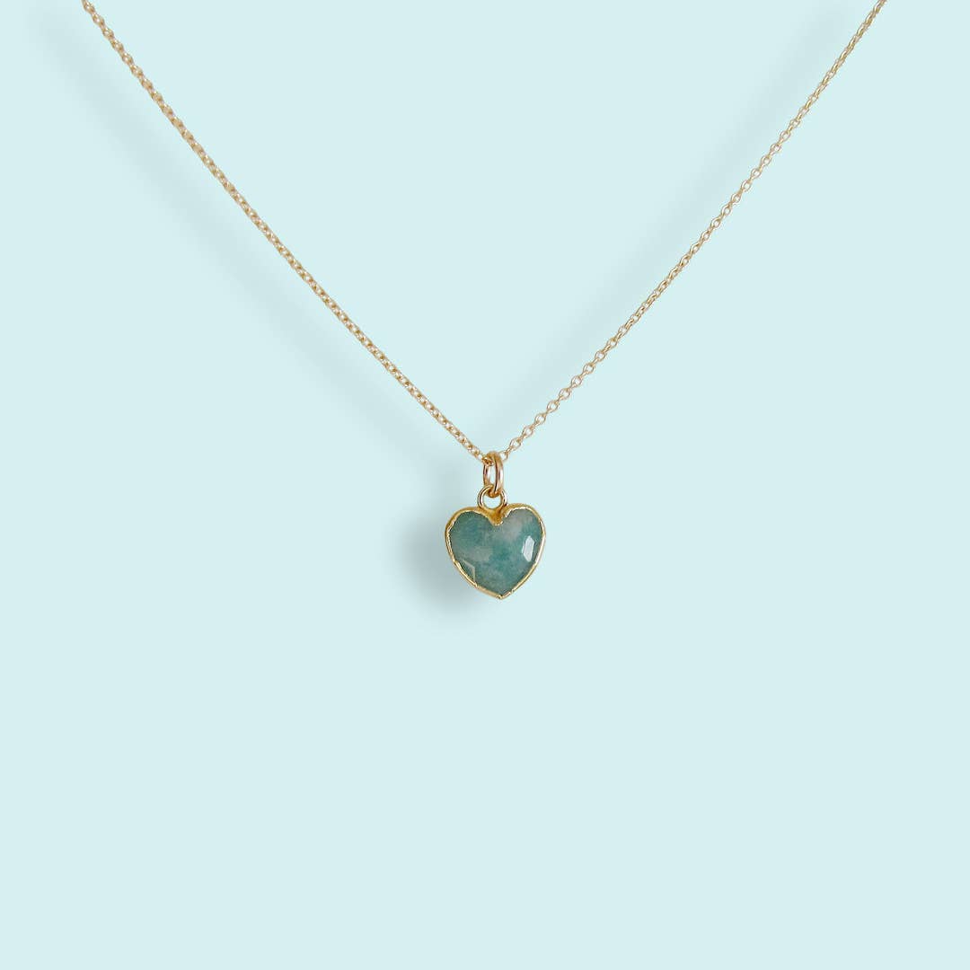 Heart-shaped green gemstone pendant on a gold chain against a light blue background
