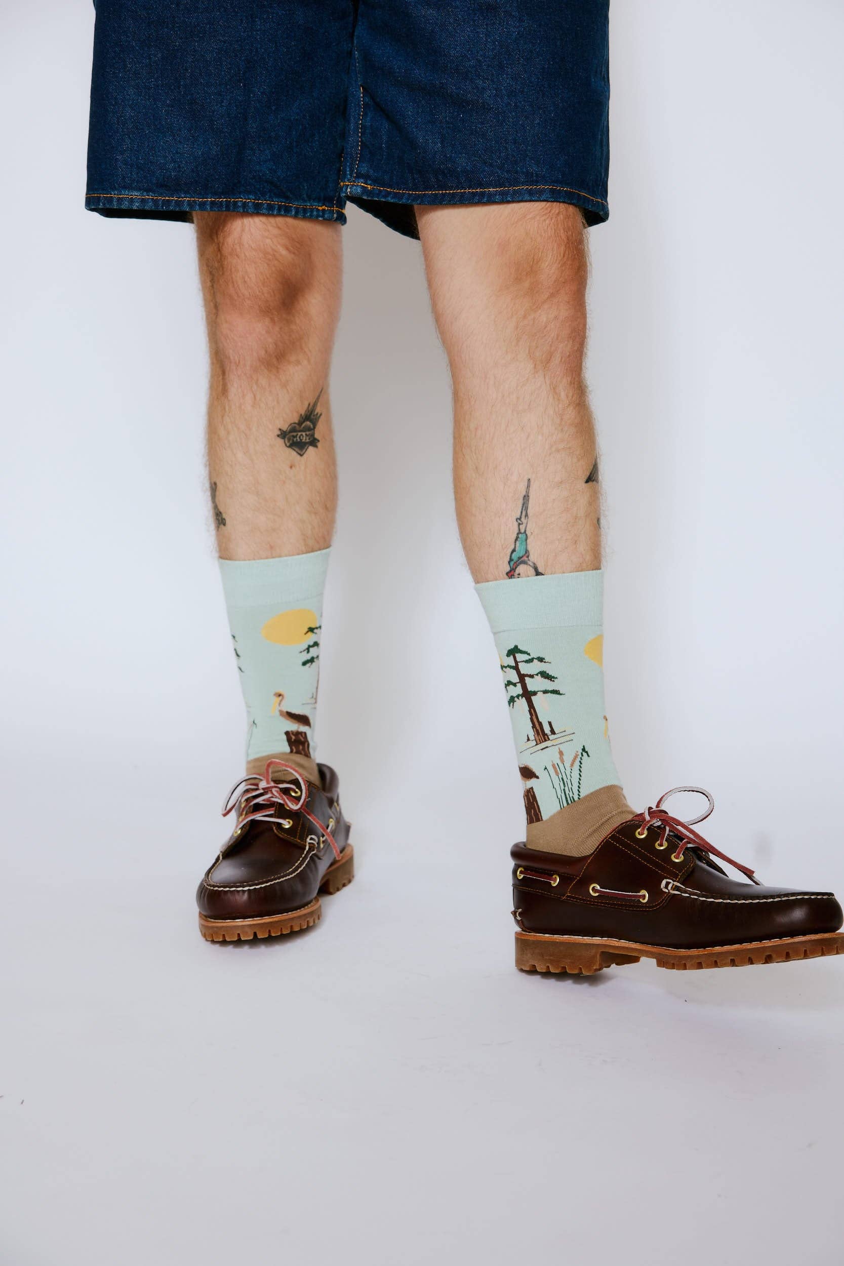 Person wearing socks with nature design and brown shoes on a white background