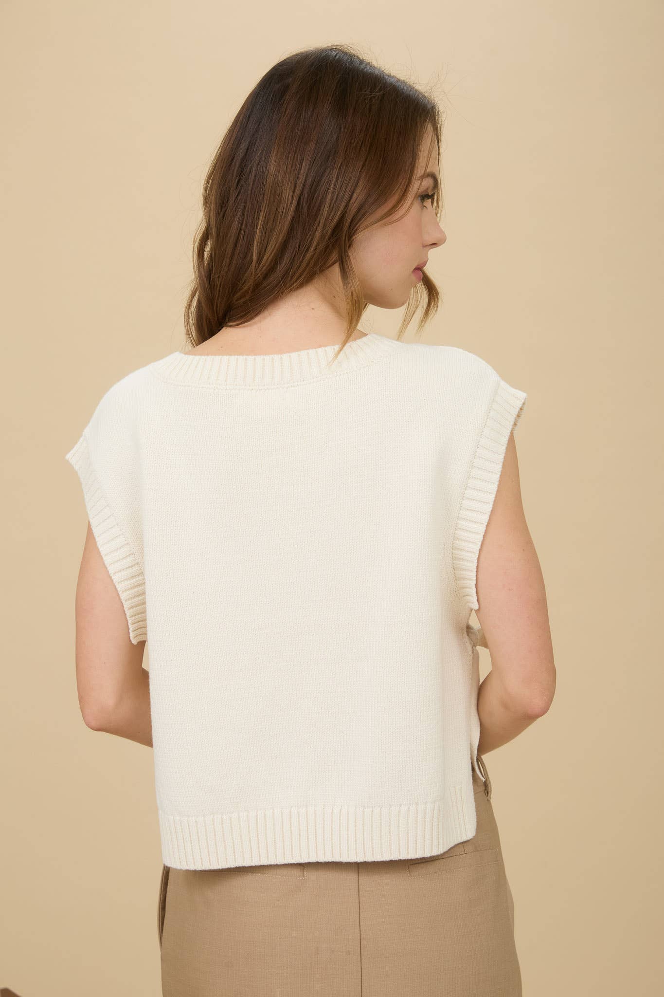 Woman wearing a cream-colored sleeveless sweater against a beige background