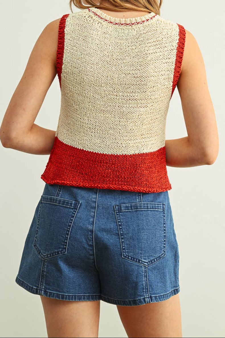 Person wearing a red and beige sleeveless top with denim shorts on a plain background