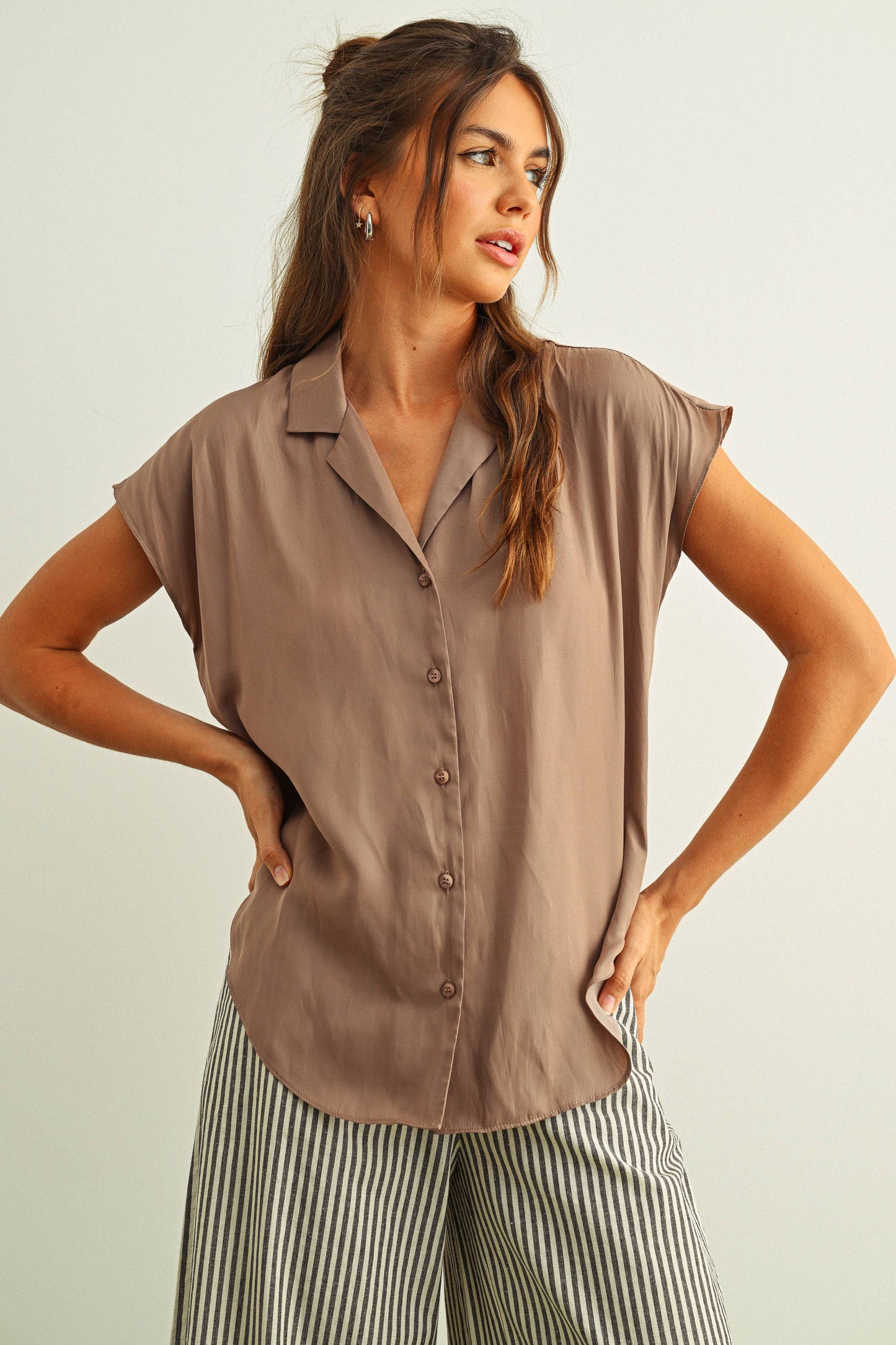 Woman wearing a brown sleeveless blouse and striped pants against a plain background