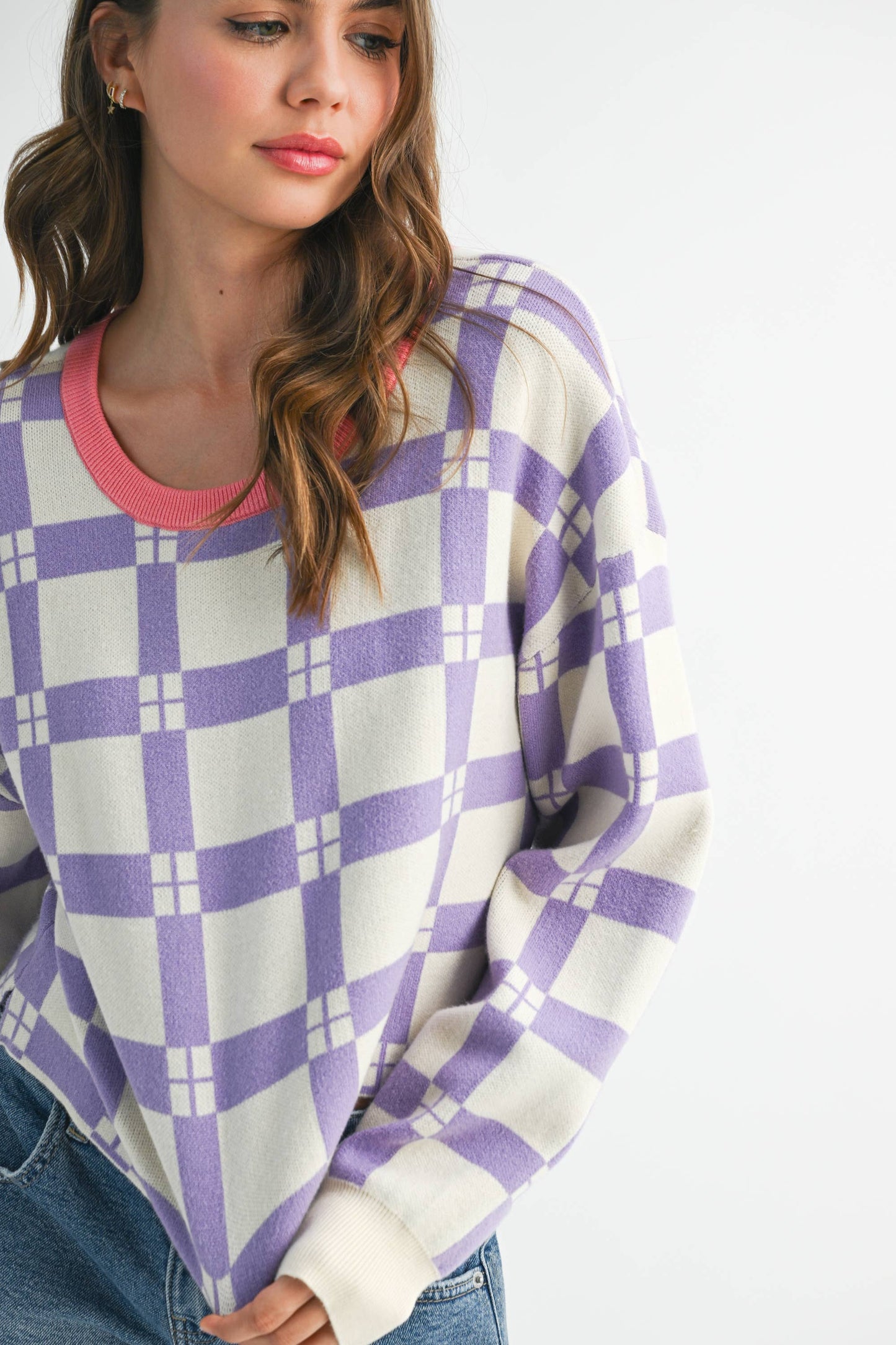Woman wearing a purple and white checkered sweater with a pink collar on a white background