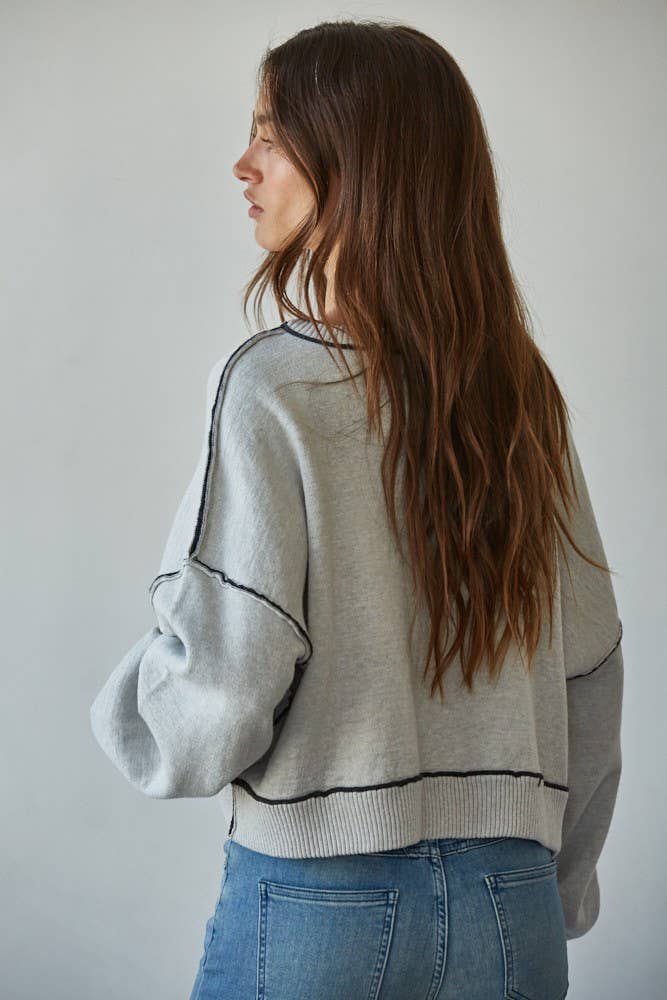 Woman wearing a light gray sweater with black accents and blue jeans against a plain background