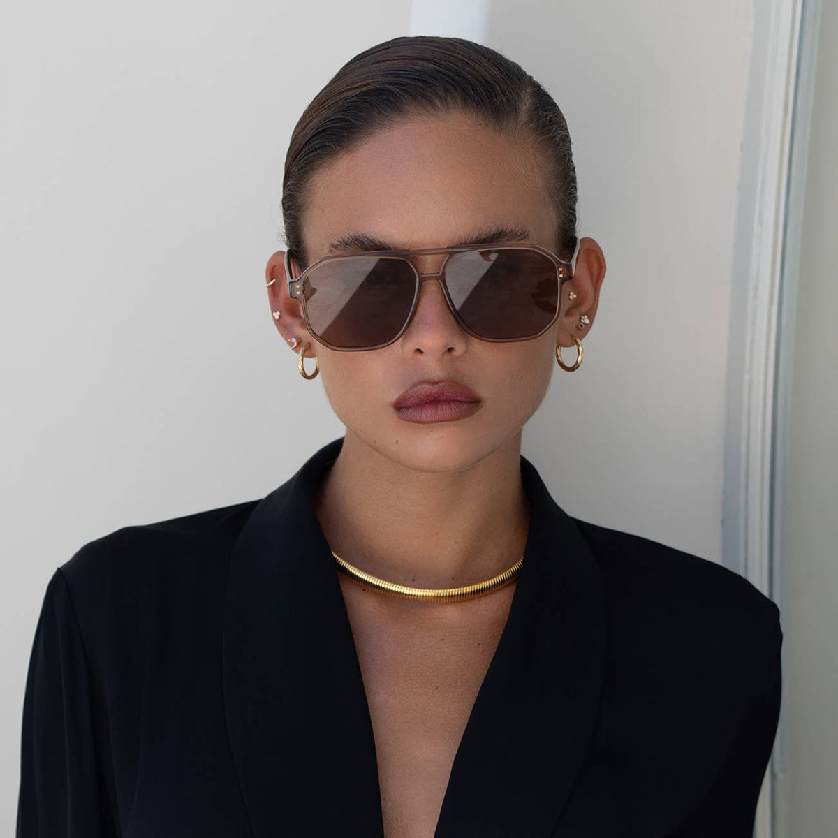 Woman wearing sunglasses and a black outfit against a plain background