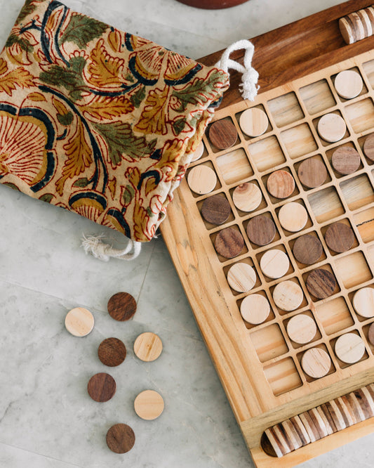 Wooden game board with wooden pieces and a patterned bag on a light surface
