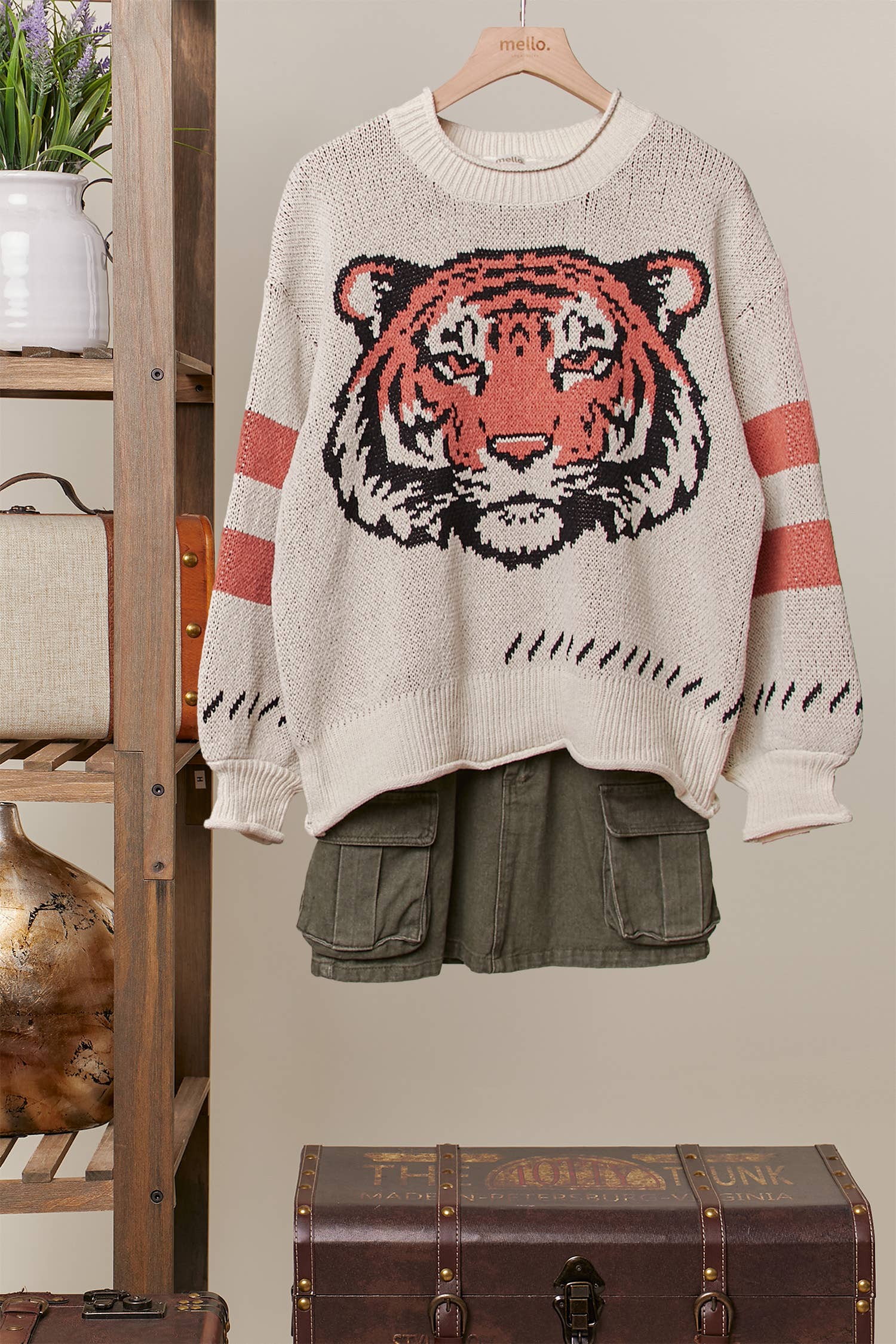 Sweater with tiger design hanging on a wooden hanger against a neutral background.