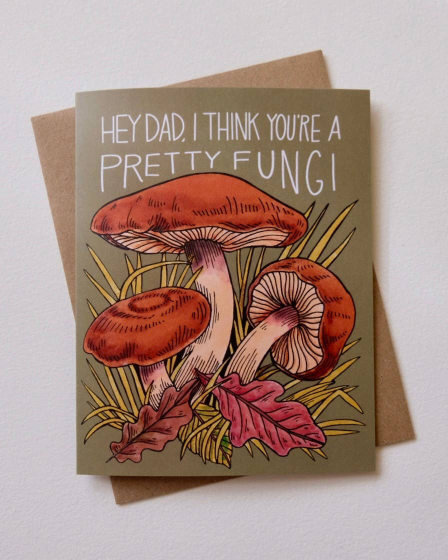 Greeting card with mushrooms and text 'Hey Dad, I think you're a pretty fungi' on a beige background.
