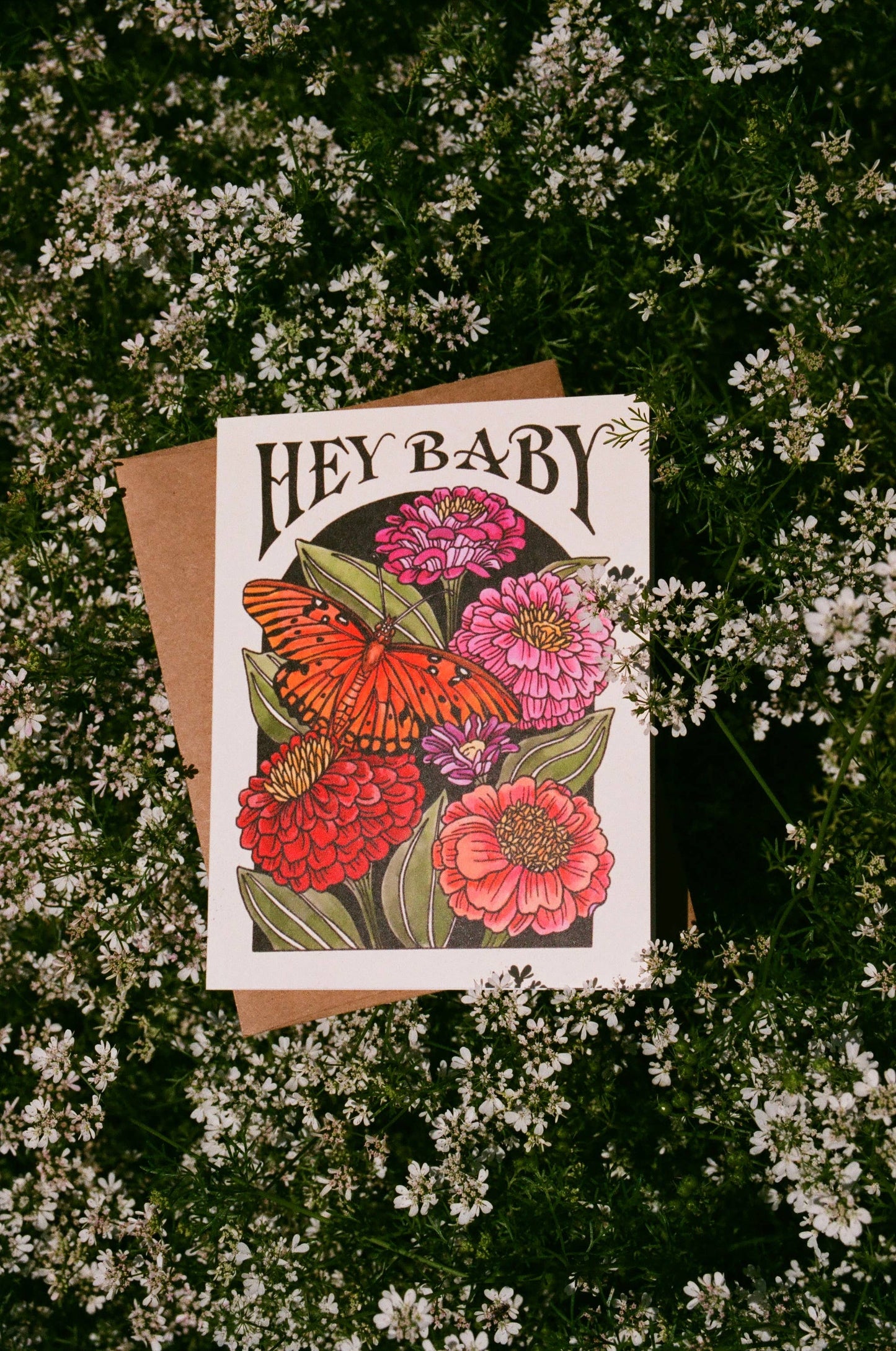 Greeting card with floral design and 'Hey Baby' text on a bed of small white flowers.